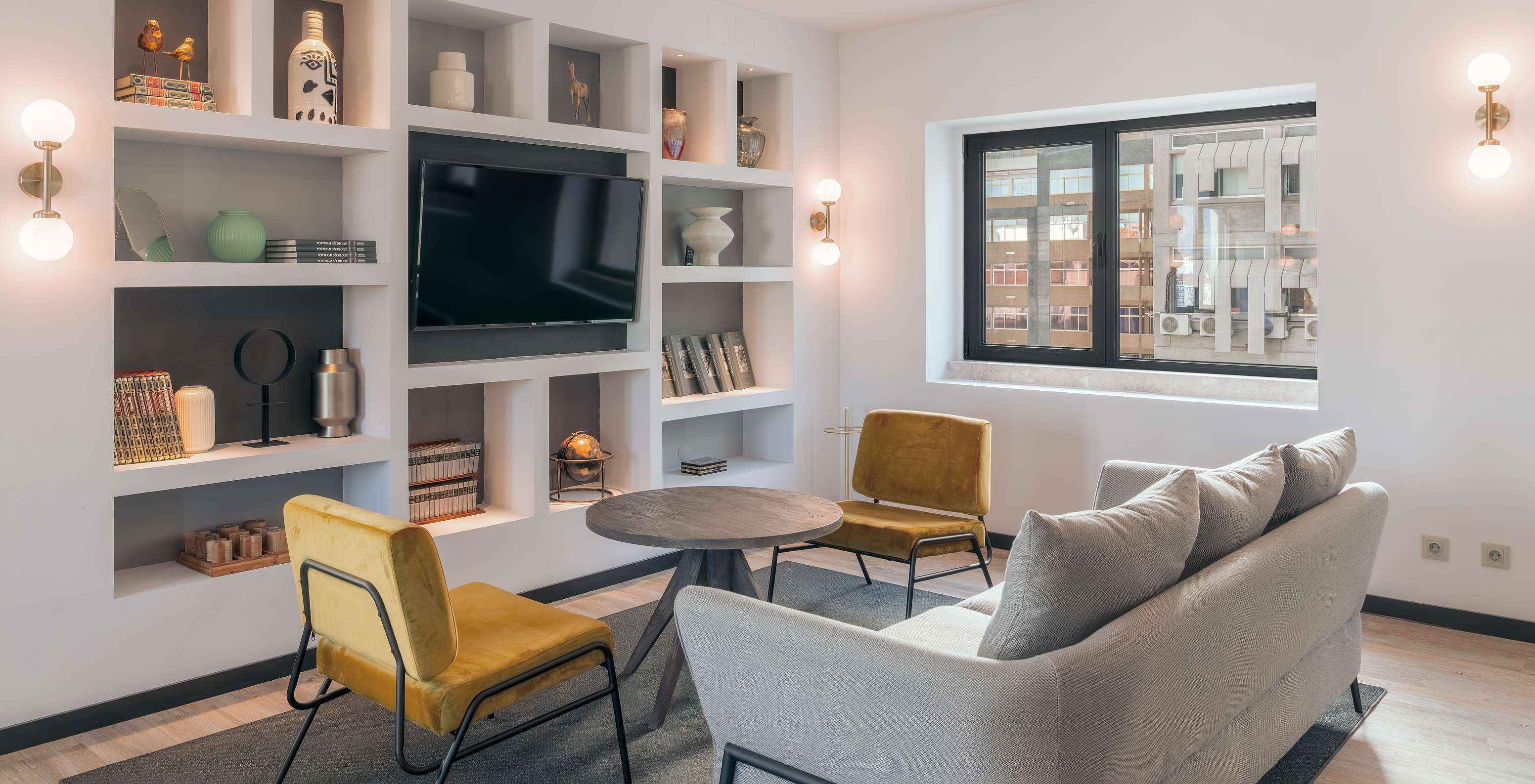 Lounge com sofá, cadeiras, mesa de apoio, televisão, tapete e objetos de decoração com janelas com vista para a cidade