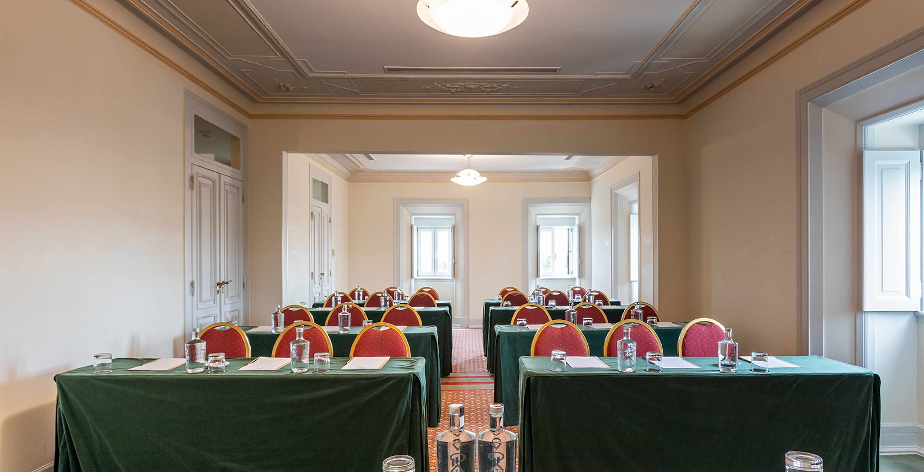 O Pestana Palace Lisboa tem uma sala de reuniões luminosa com várias mesas verdes e cadeiras vermelhas