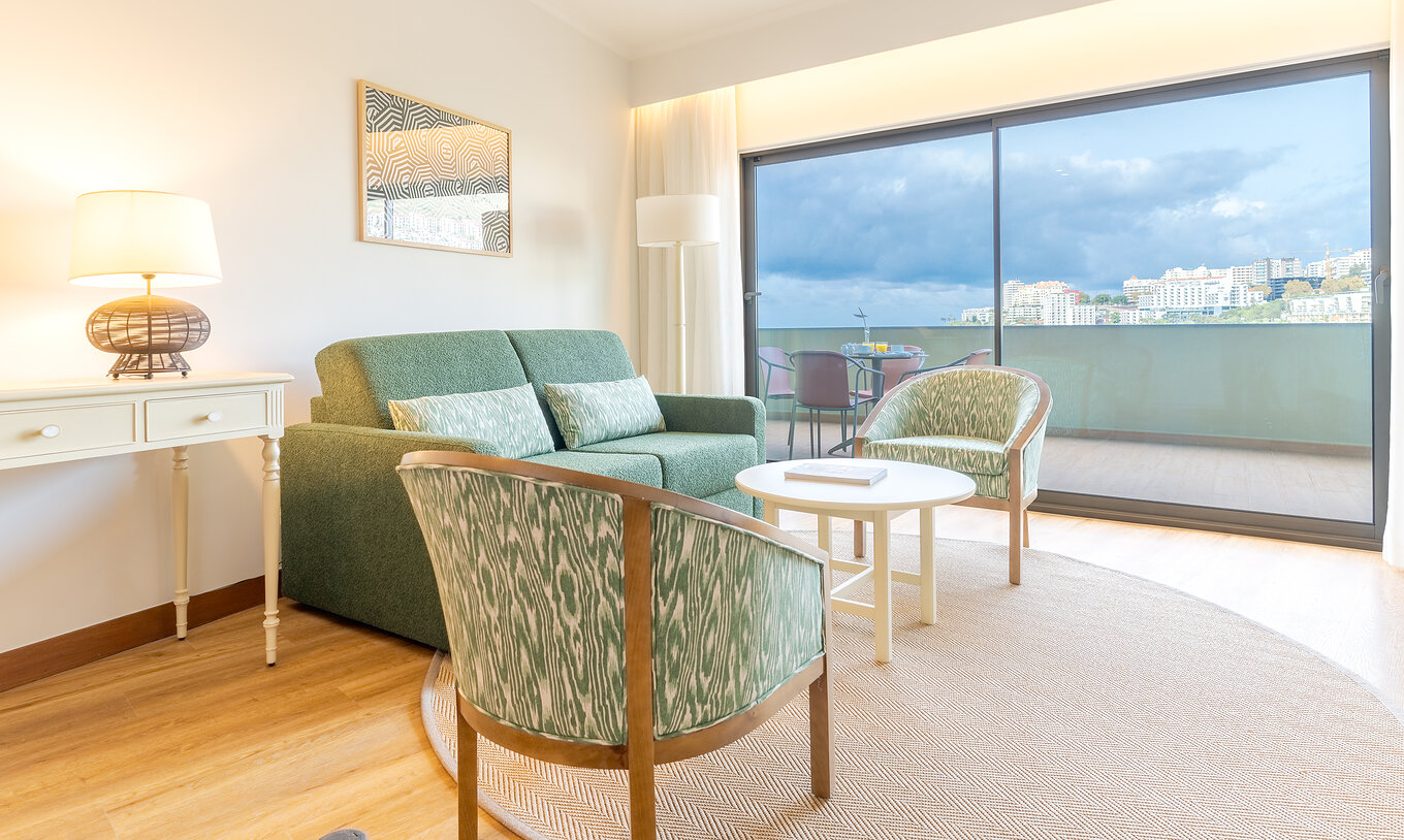 A Suite Superior Vista Mar Lateral do Pestana Vila Lido Madeira tem uma sala de estar com sofá, cadeirões e varanda