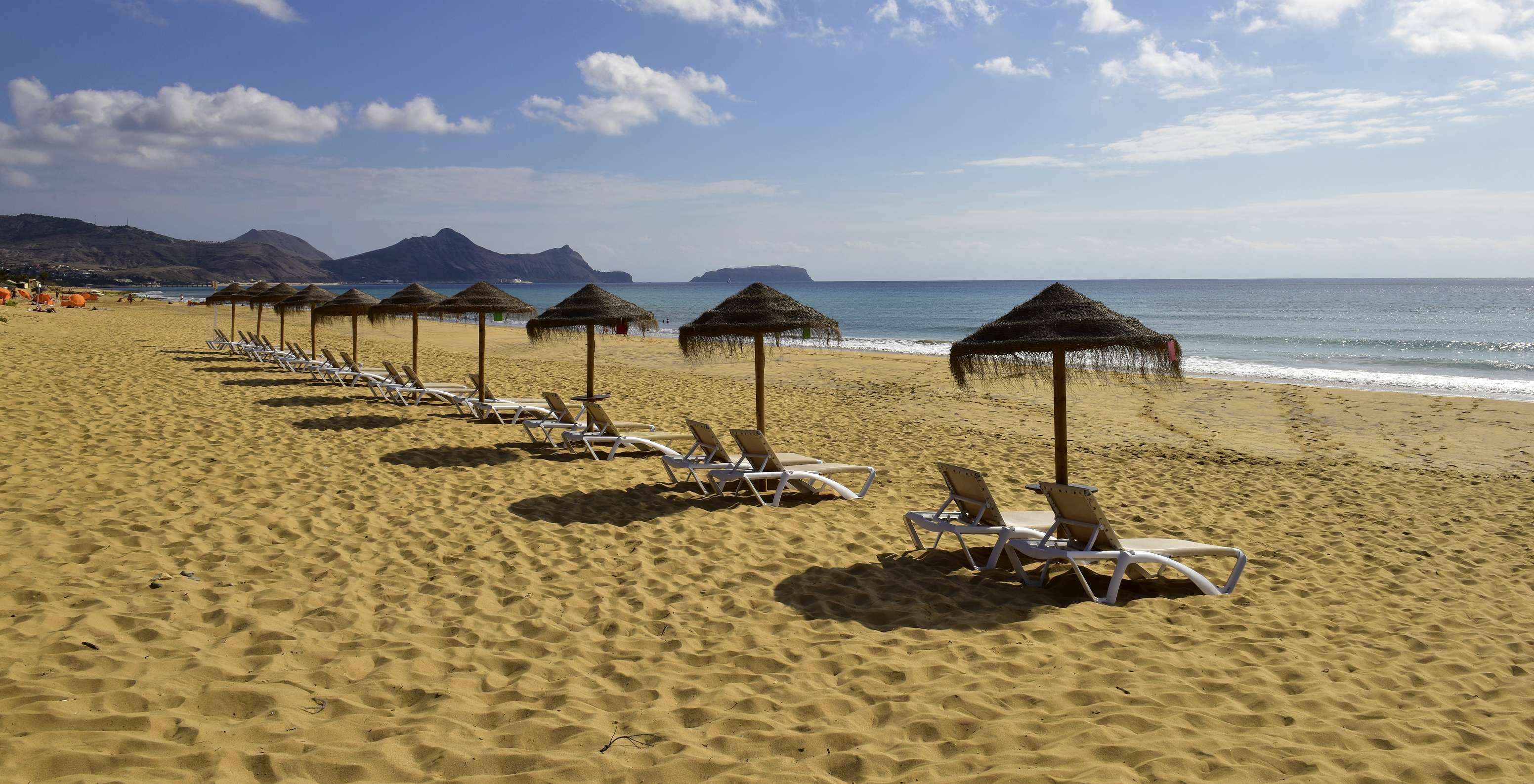 Praia do de areia fina, mar azul e montanhas ao fundo, do Pestana Porto Santo, Hotel com Tudo Incluído e Spa no Porto Santo
