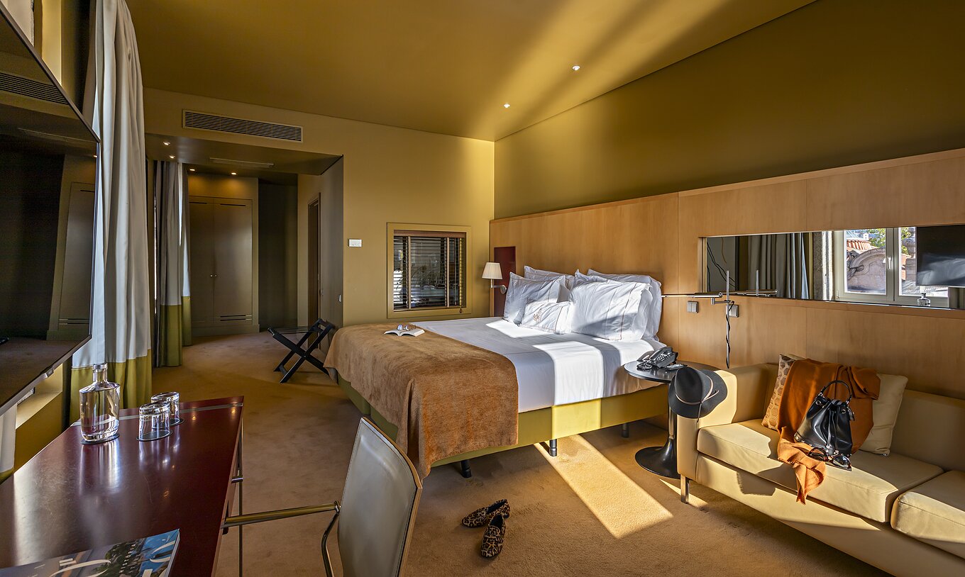 O Deluxe Grand View do Pestana Palácio do Freixo tem uma cama de casal com uma manta camel, um sofá e uma secretária