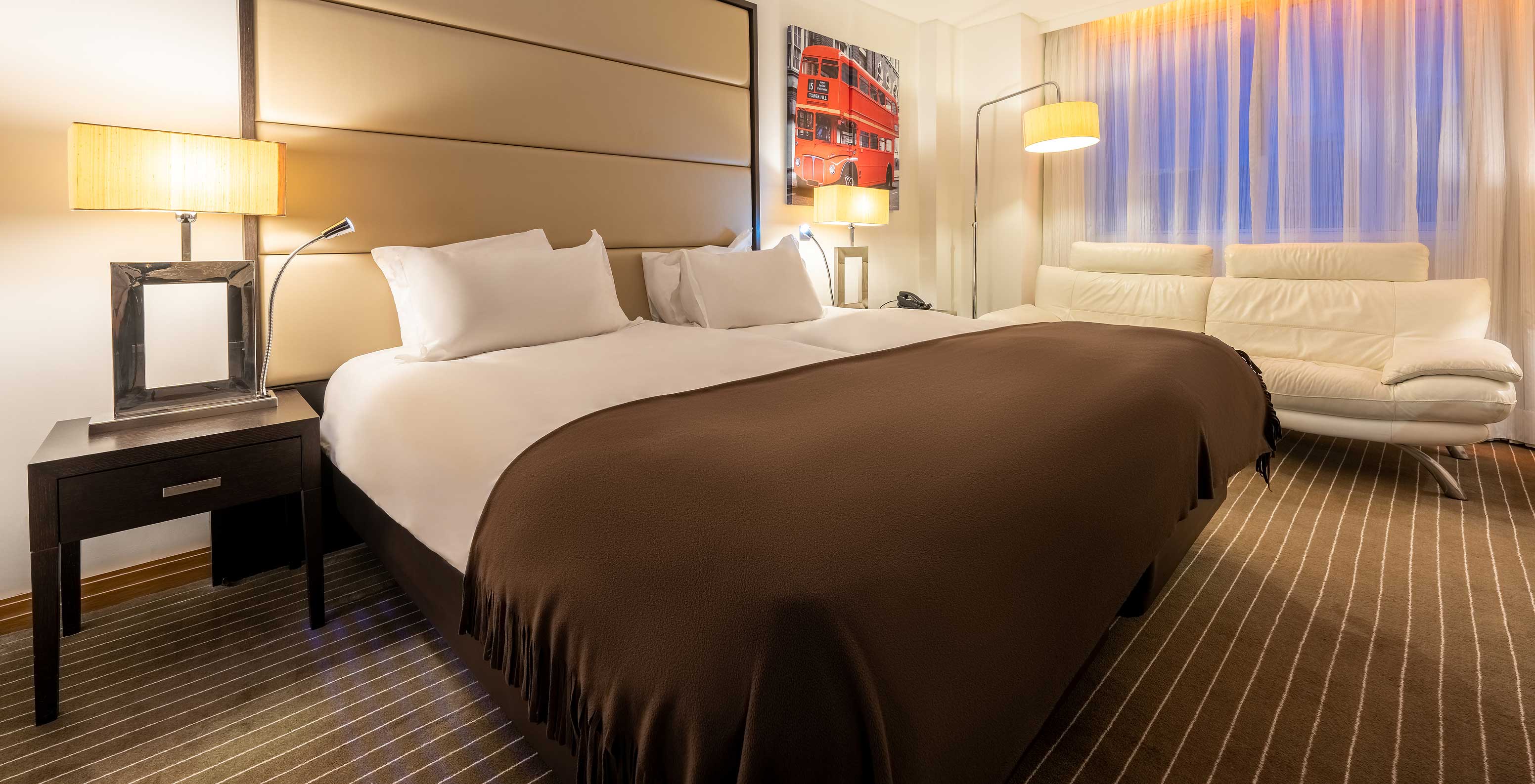 O Premium Twin do Pestana Chelsea Bridge tem duas camas juntas, mesa de cabeceira, sofá, candeeiros e janelas com cortinados