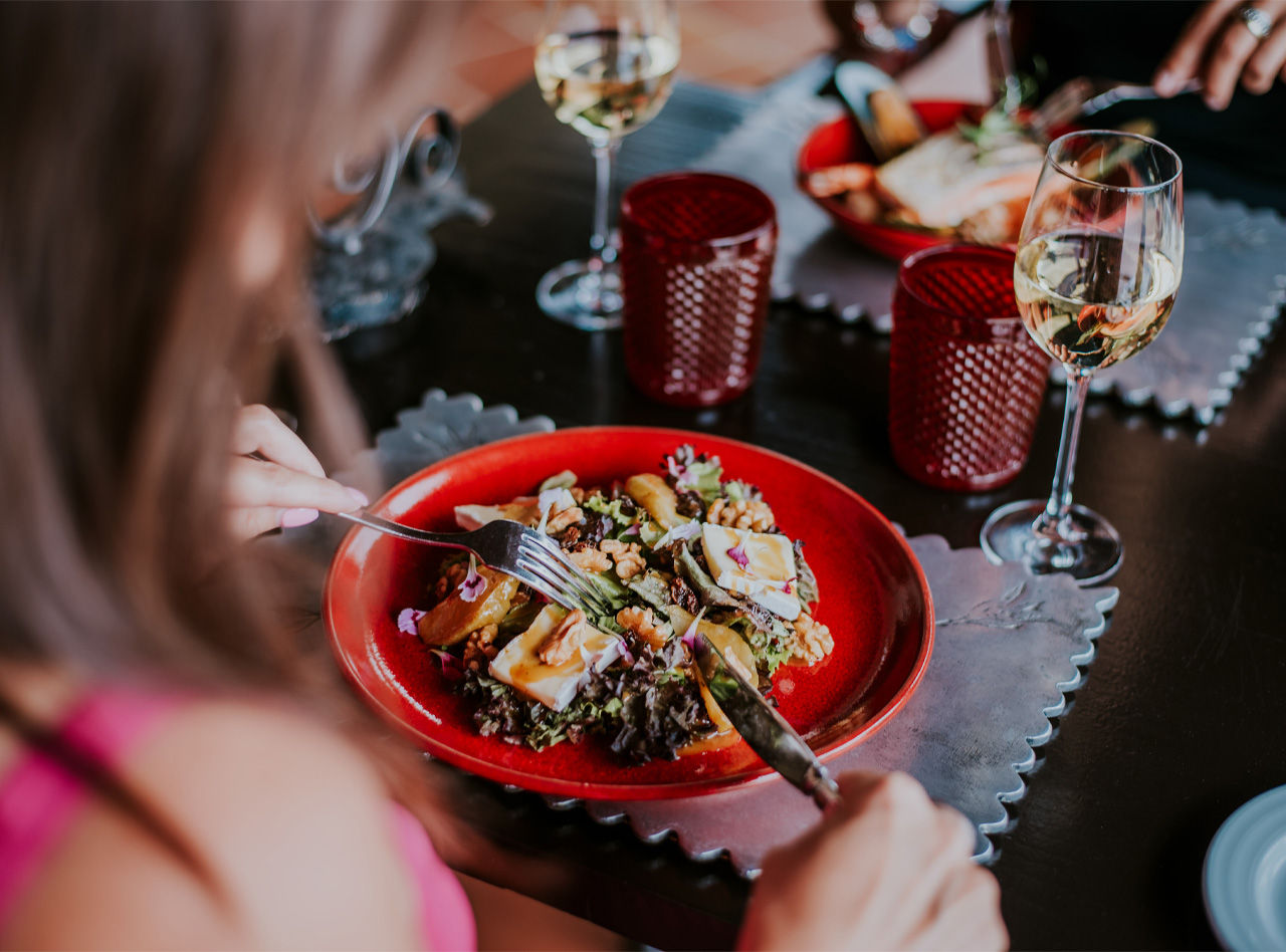 Roter Teller mit Salat und einem Glas Weißwein, während einer Mahlzeit in einem Hotel der Pestana Hotels and Resorts