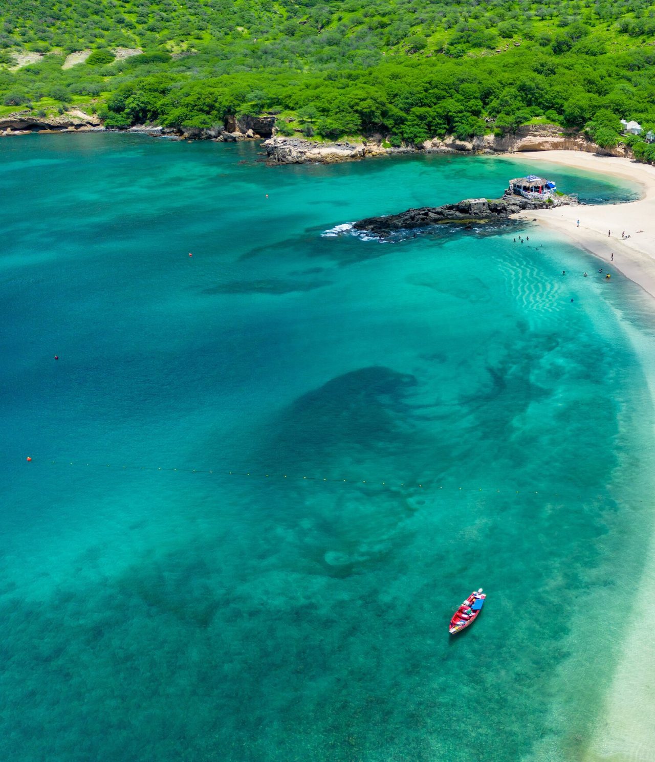 Paradiesstrand mit kristallklarem türkisfarbenem Wasser und weißem Sand, mit bunten Booten an der Küste