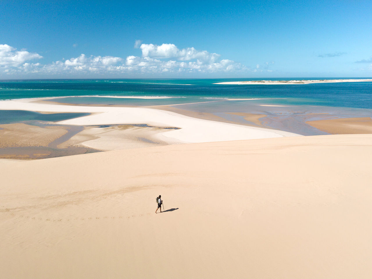 Ein einsamer Wanderer, der über die weiten weißen Sanddünen von Bazaruto geht, mit dem Indischen Ozean im Hintergrund