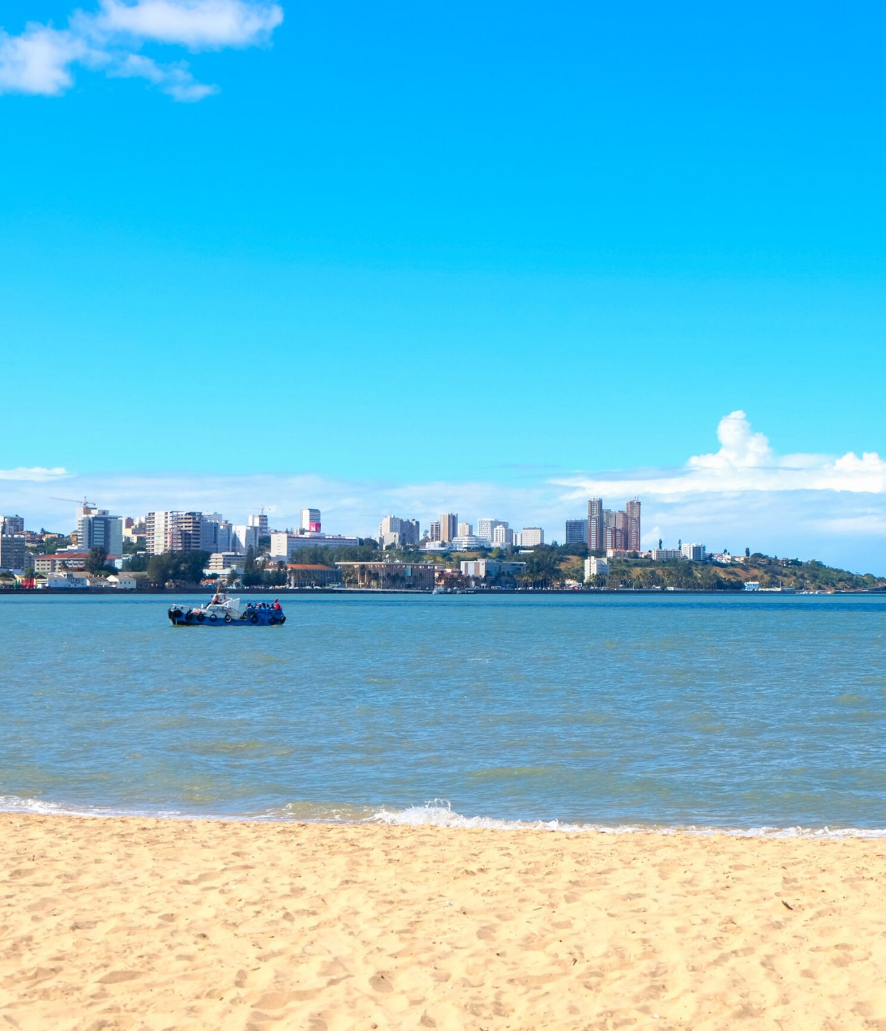 Blick über die Stadt Maputo vom anderen Flussufer, an einem Strand, wo mehrere Kinder im Wasser spielen