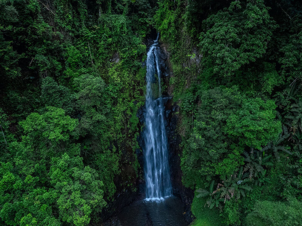 Langer Wasserfall mitten in dichter Vegetation, der in einen kleinen See in São Tomé mündet