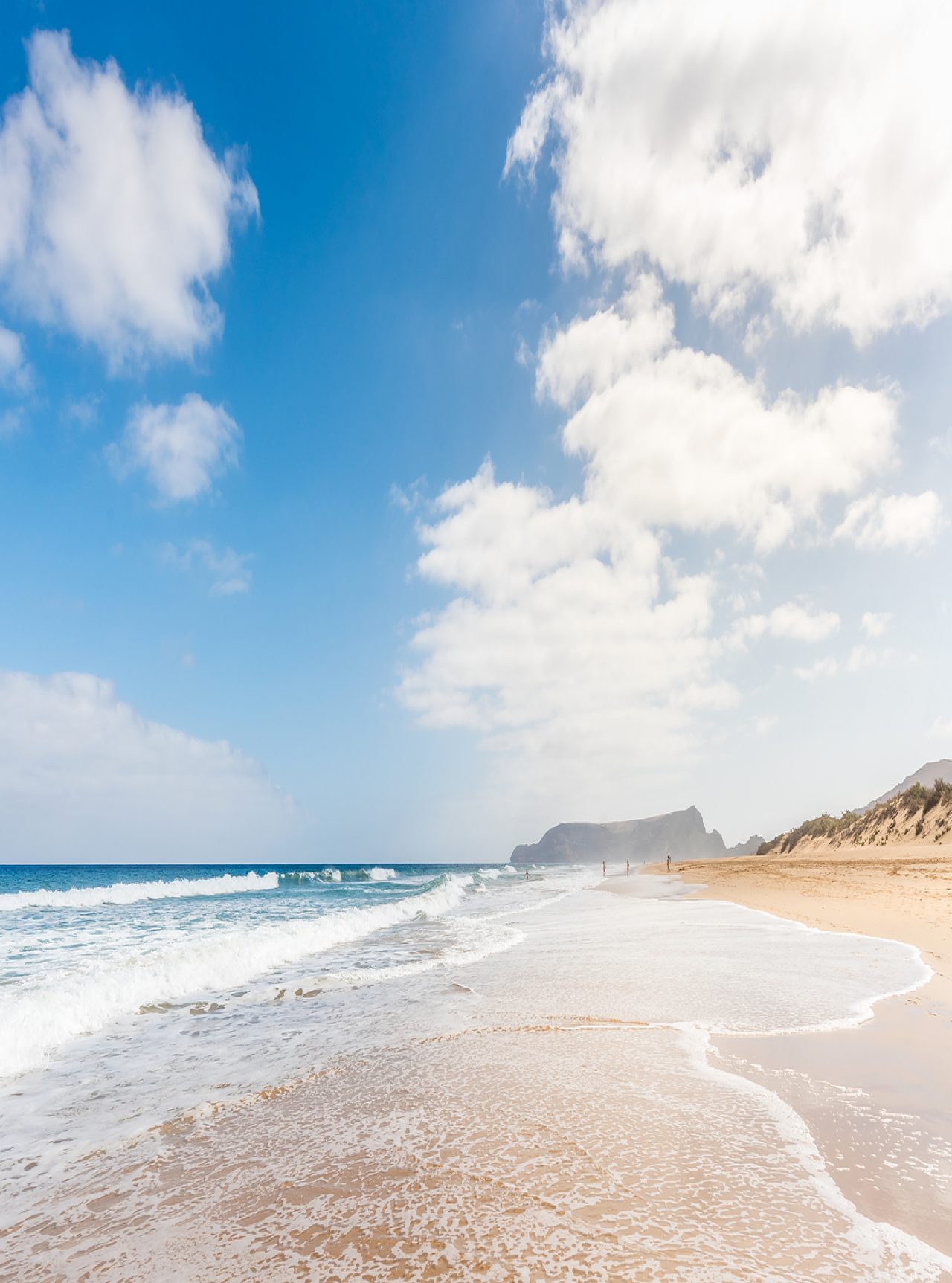 Langer Strand in Porto Santo mit hellem Sand, ruhigen Wellen und blauem Himmel mit einigen Wolken