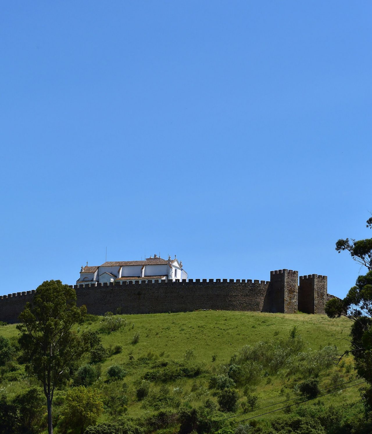 Historisches Schloss auf einem Hügel in Arraiolos, Alentejo, umgeben von grünen Landschaften und klarem blauen Himmel