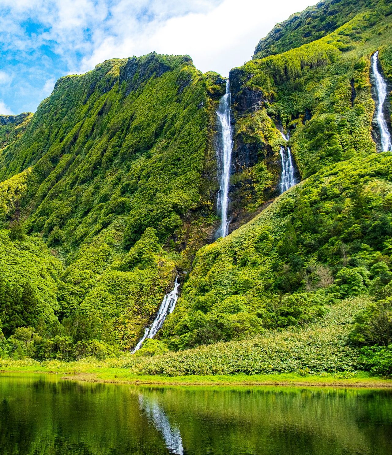 Atemberaubender Wasserfall, umgeben von grünbewachsenen Bergen auf der Insel Flores, Azoren