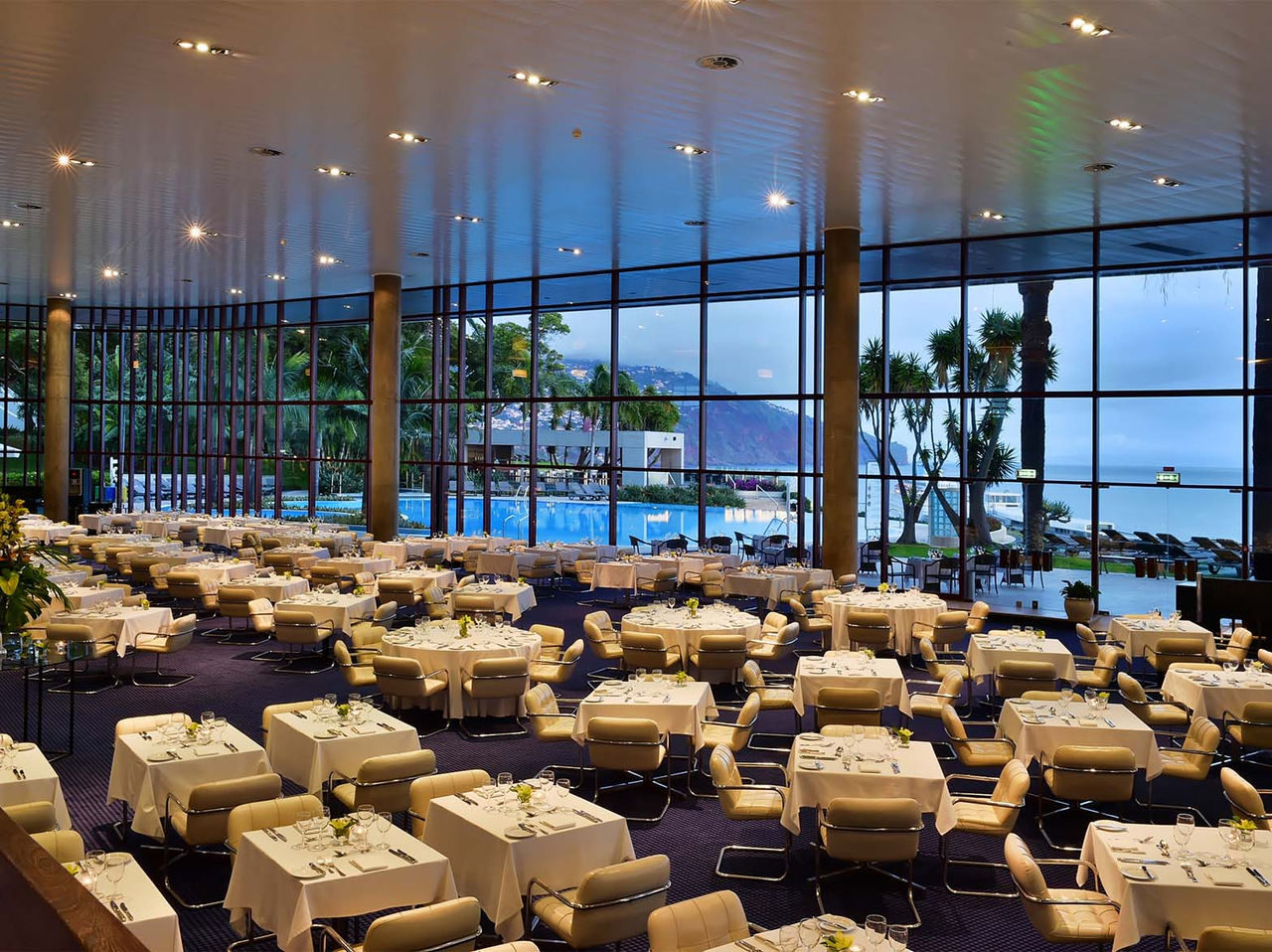 Das Restaurant Panorâmico im Hotel in Funchal, Madeira, hat mehrere Tische und gepolsterte Stühle in Beige