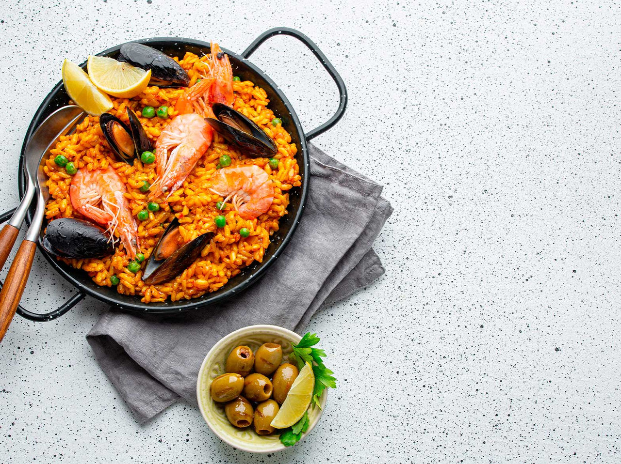 Typisches spanisches Gericht, eine Pfanne Paella, zubereitet mit Muscheln, Garnelen, Erbsen und Reis, serviert mit Oliven