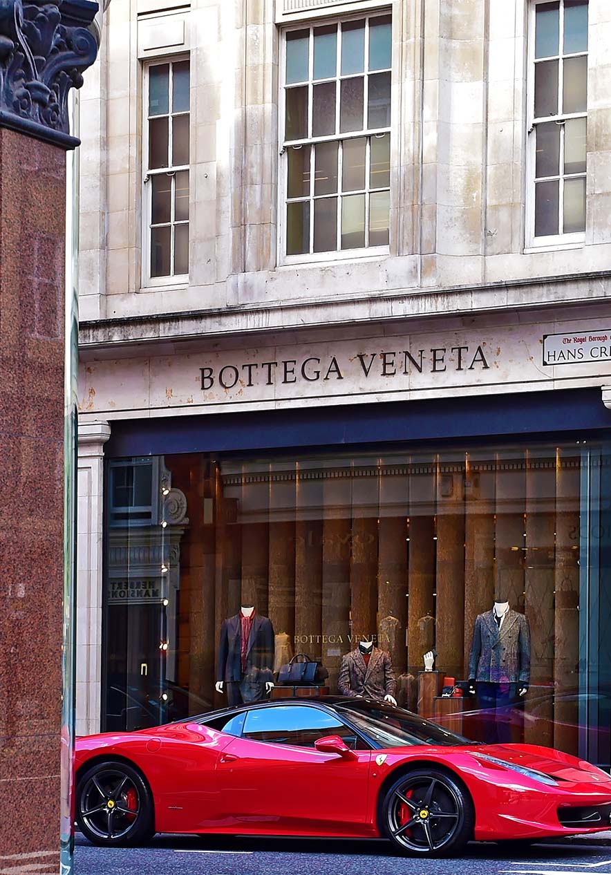Luxusgeschäftstraße mit Schuhen und Accessoires im Schaufenster, roter Ferrari auf der Seitenstraße