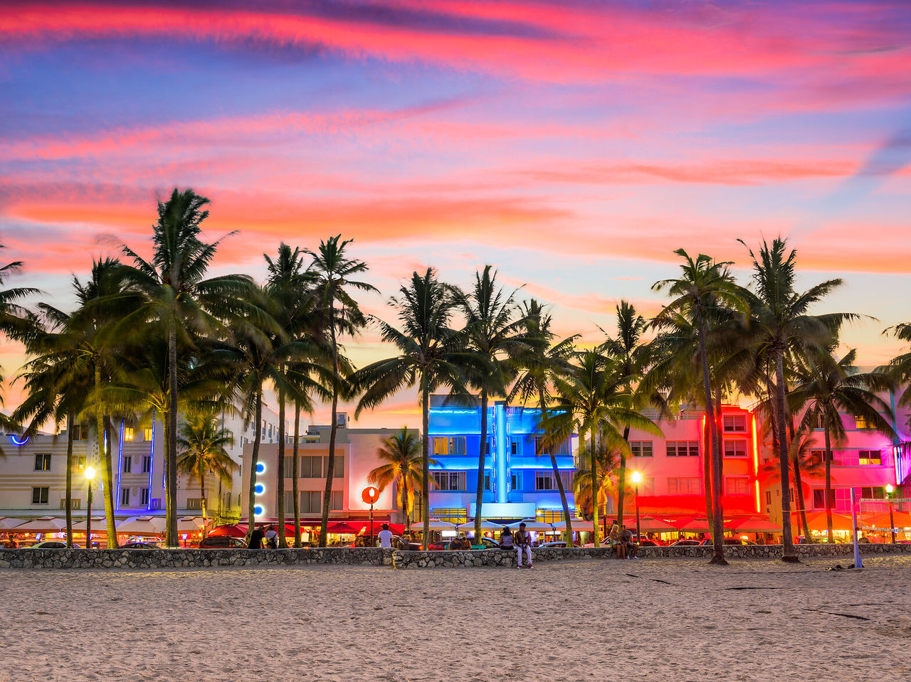 Lebhafter Sonnenuntergang in Miami Beach, mit silhouettierten Palmen und beleuchteten Art-Deco-Gebäuden