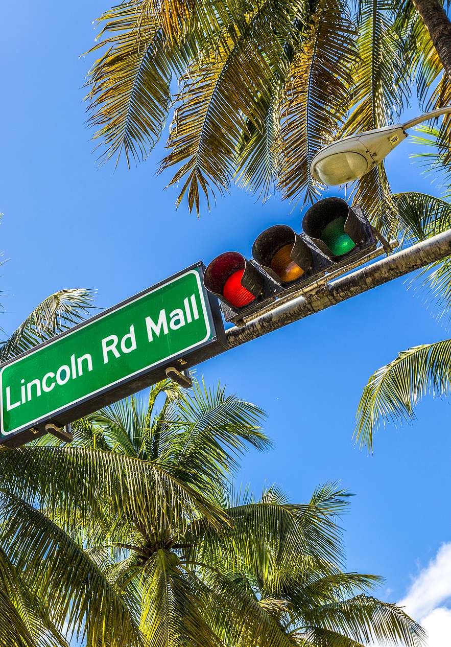 Verkehrsschild mit "Lincoln Rd Mall", neben einer Ampel, umgeben von Palmen und klarem blauen Himmel