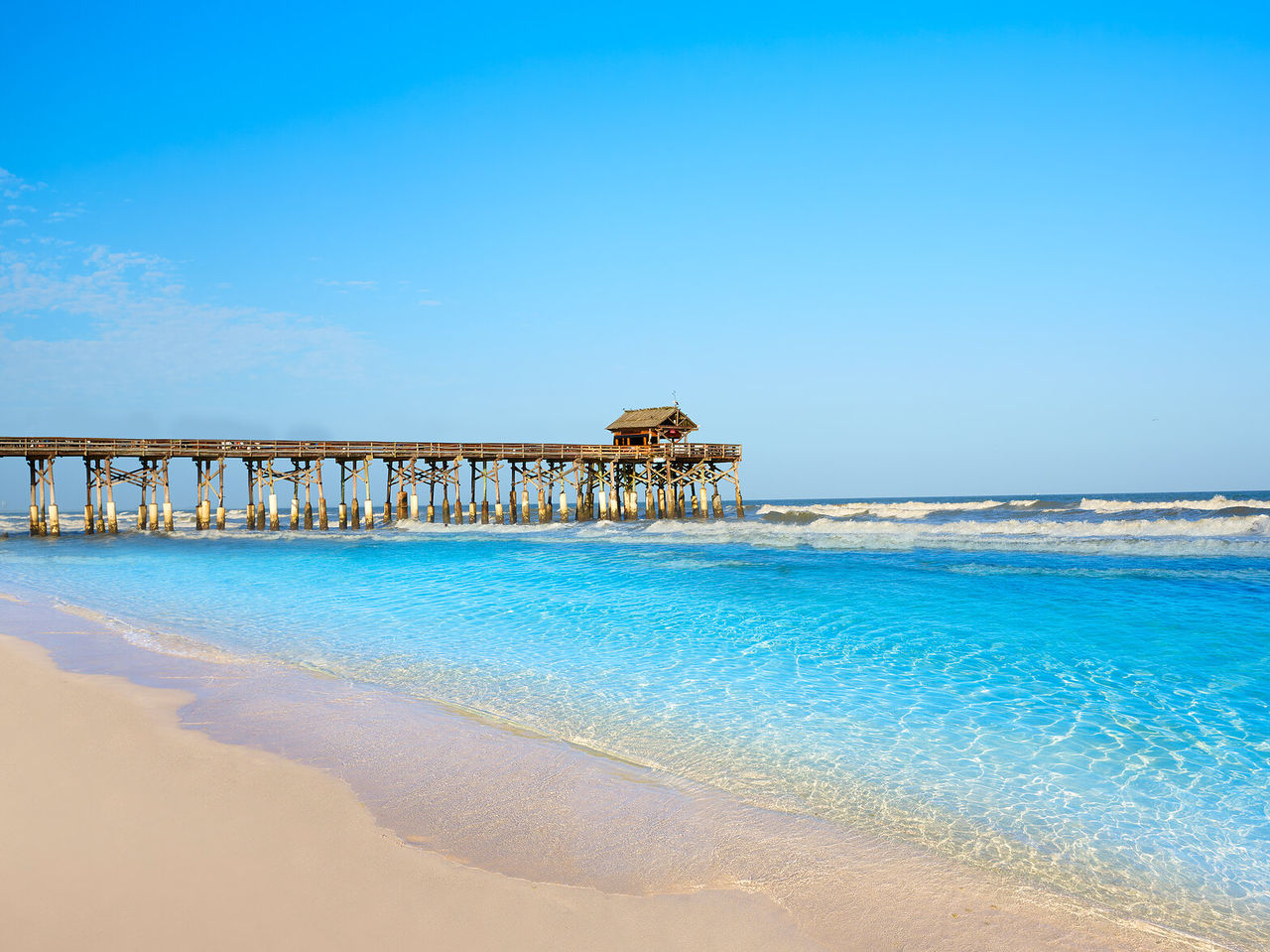 Langer Holzsteg über kristallklarem Wasser, der einen Blick auf einen weißen Sandstrand mit einem entspannenden Meer bietet