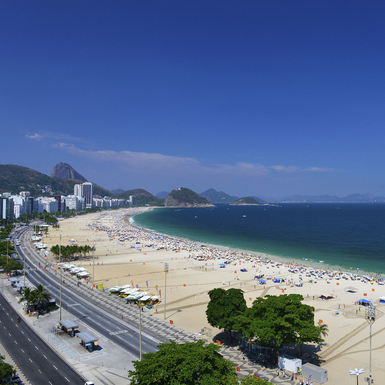 Copacabana-Strand in Rio de Janeiro, belebter Strand mit goldenem Sand, blauem Meer und Bergen im Hintergrund