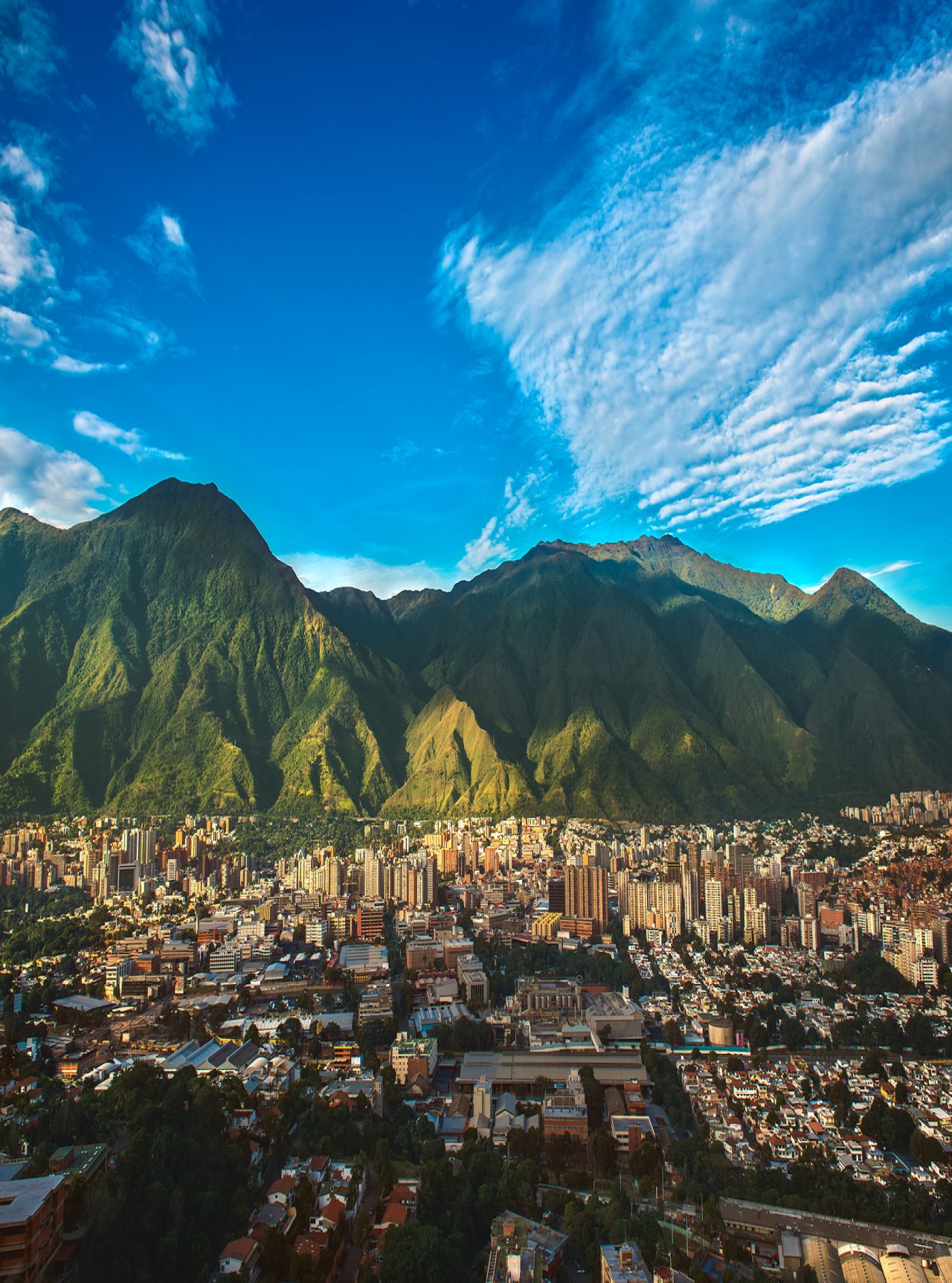 Luftaufnahme der Stadt Caracas mit hohen Gebäuden, die im Gegensatz zur bergigen Natur und dem blauen Himmel stehen