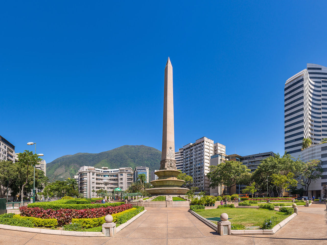 Obelisk-Denkmal, große Steinsäule in der Mitte eines Parks mit Blumen, umgeben von hohen Gebäuden in Caracas