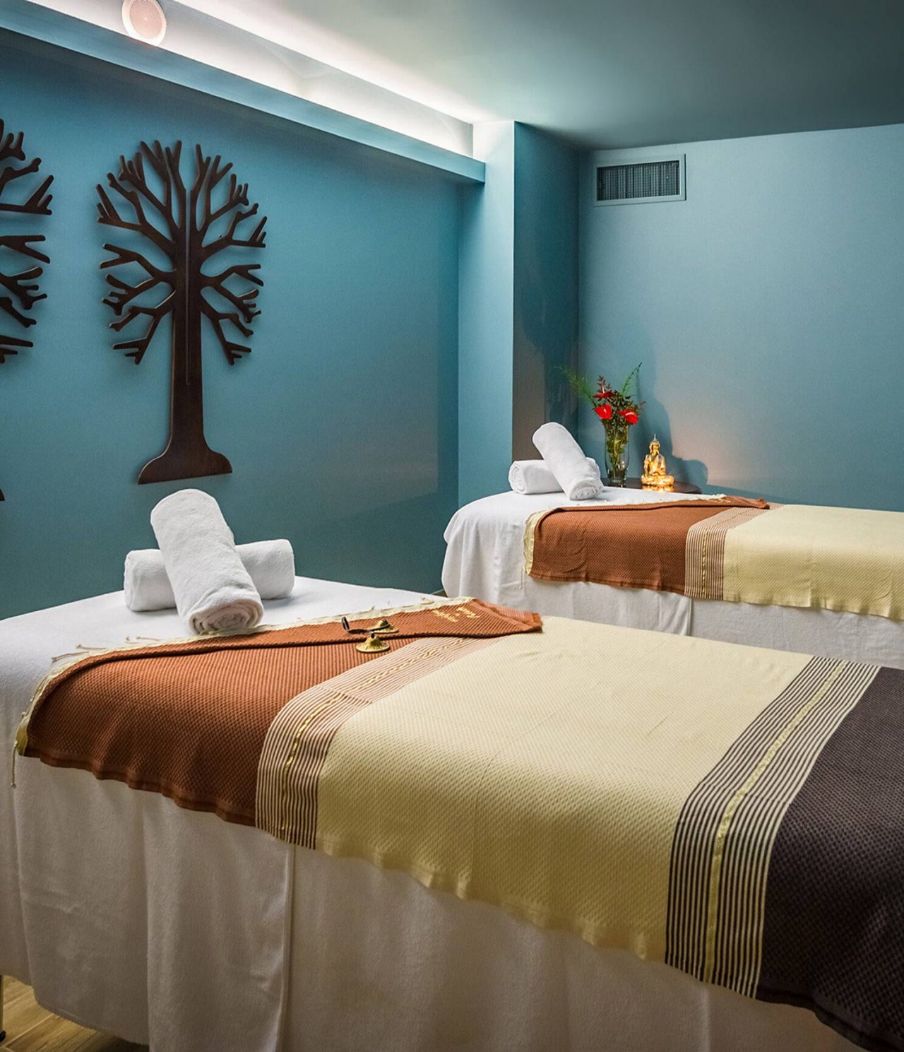 Spa-Raum im Pestana Magic Spa mit zwei Massageliegen, Kunst an den Wänden und einer Buddha-Statue auf einem Tisch mit Blumen