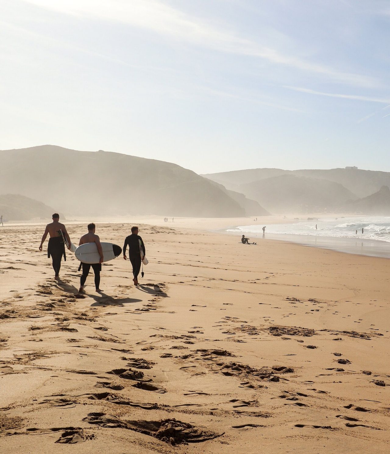 Surfers carrying their surfboard on a beach on the Algarve coast, with waves and rocks in the background