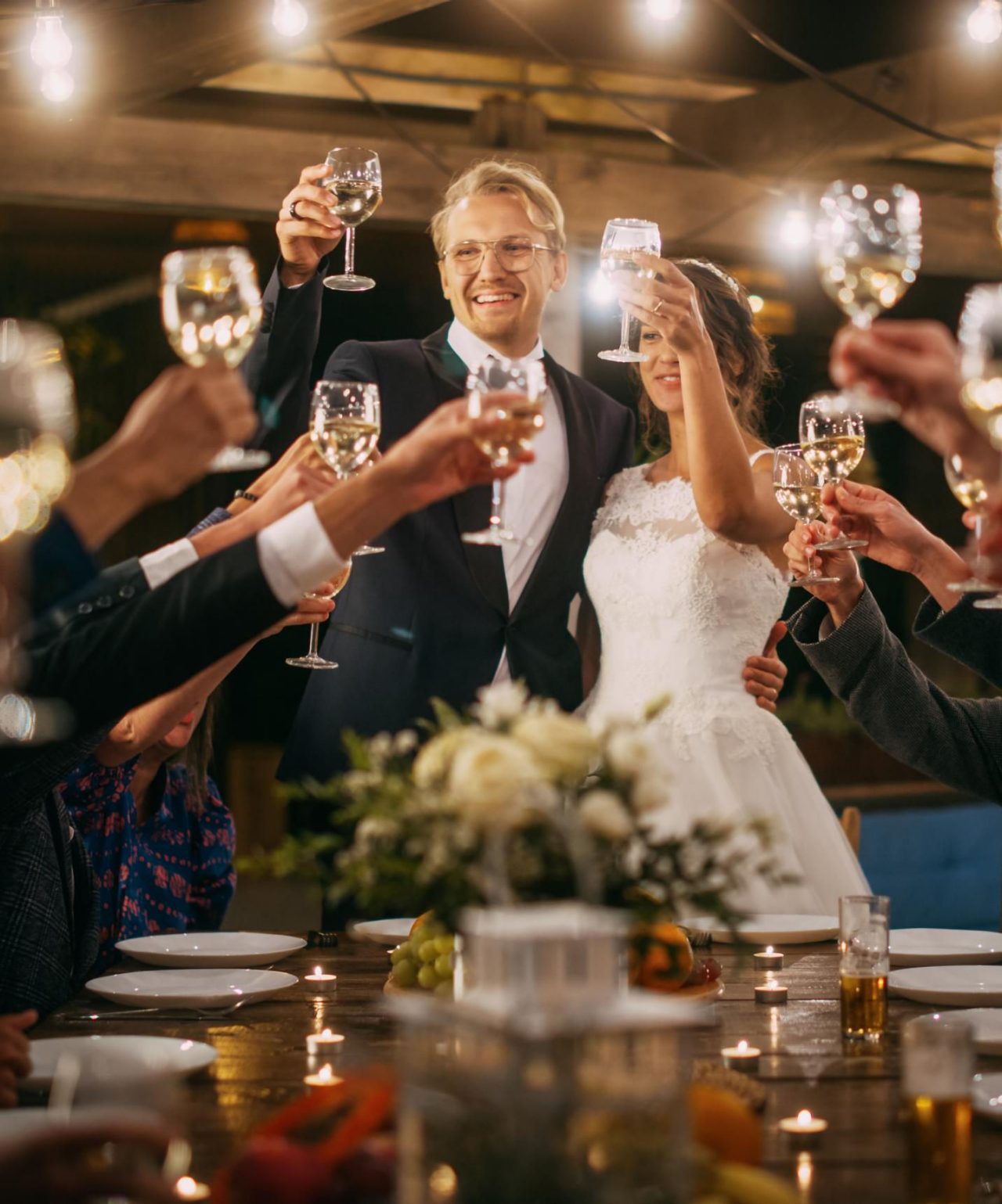 Newlyweds celebrate their wedding, toasting with their guests at an elegant table with a floral arrangement