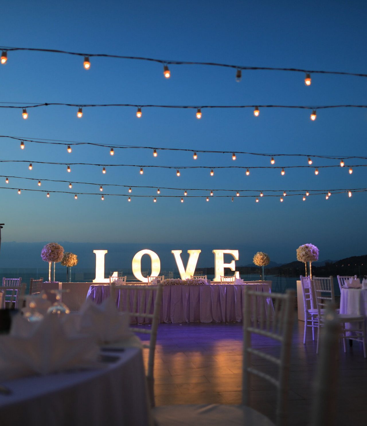 Decoration for your special occasion, with outdoor tables, hanging lights, and a large sign that says "Love"
