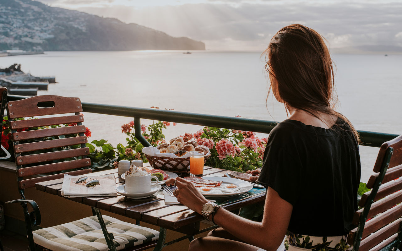 Mujer desayunando en la terraza de un restaurante con vista al océano, en un hotel junto al mar