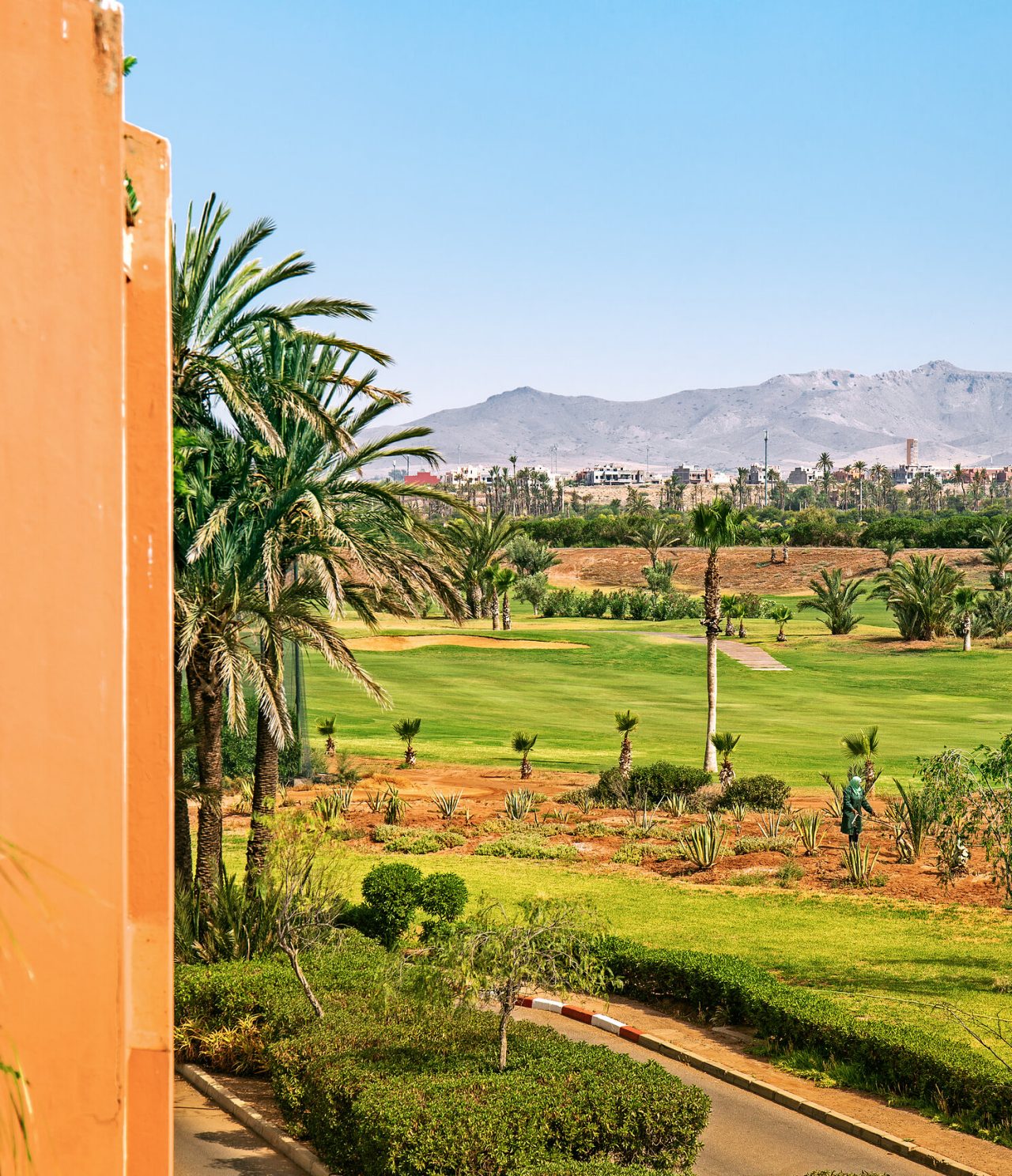 Vista desde un balcón con campos verdes y varios árboles, ciudad y montañas en el horizonte