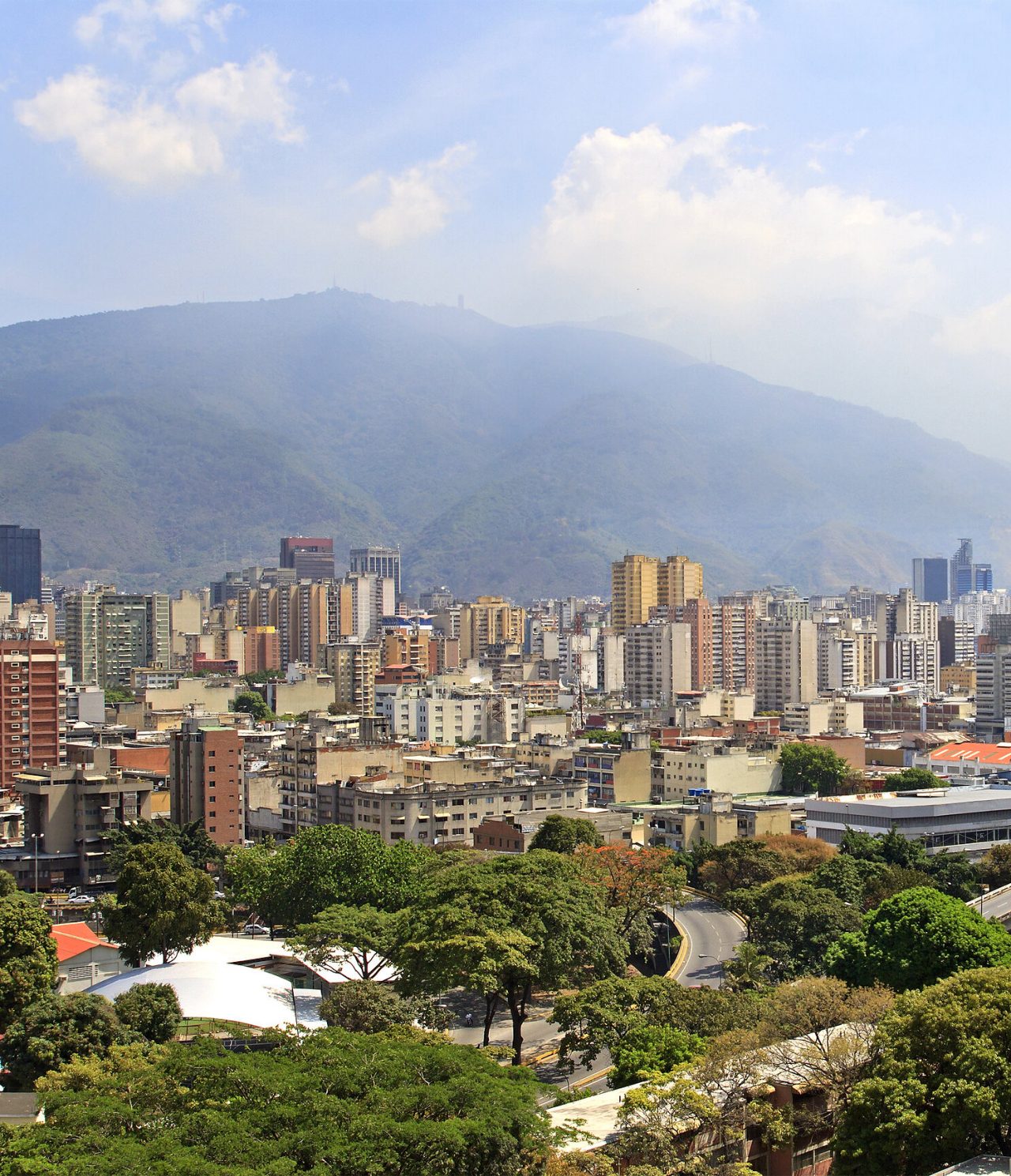 Vista aérea panorámica de Caracas, con varios edificios altos, algunas construcciones modernas y vegetación