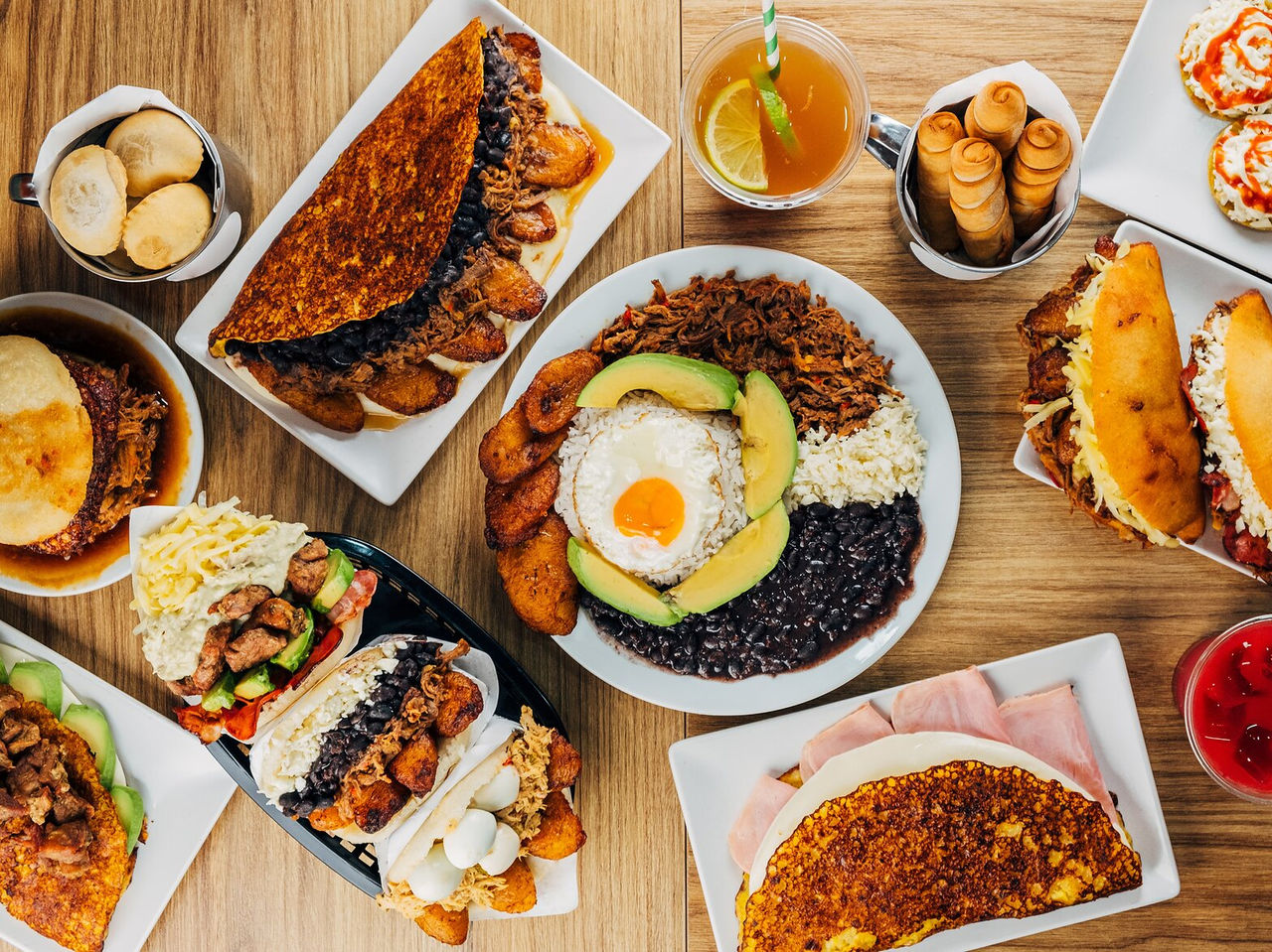 Mesa llena de platos típicos venezolanos, incluyendo arepas, tequeños y chapachas