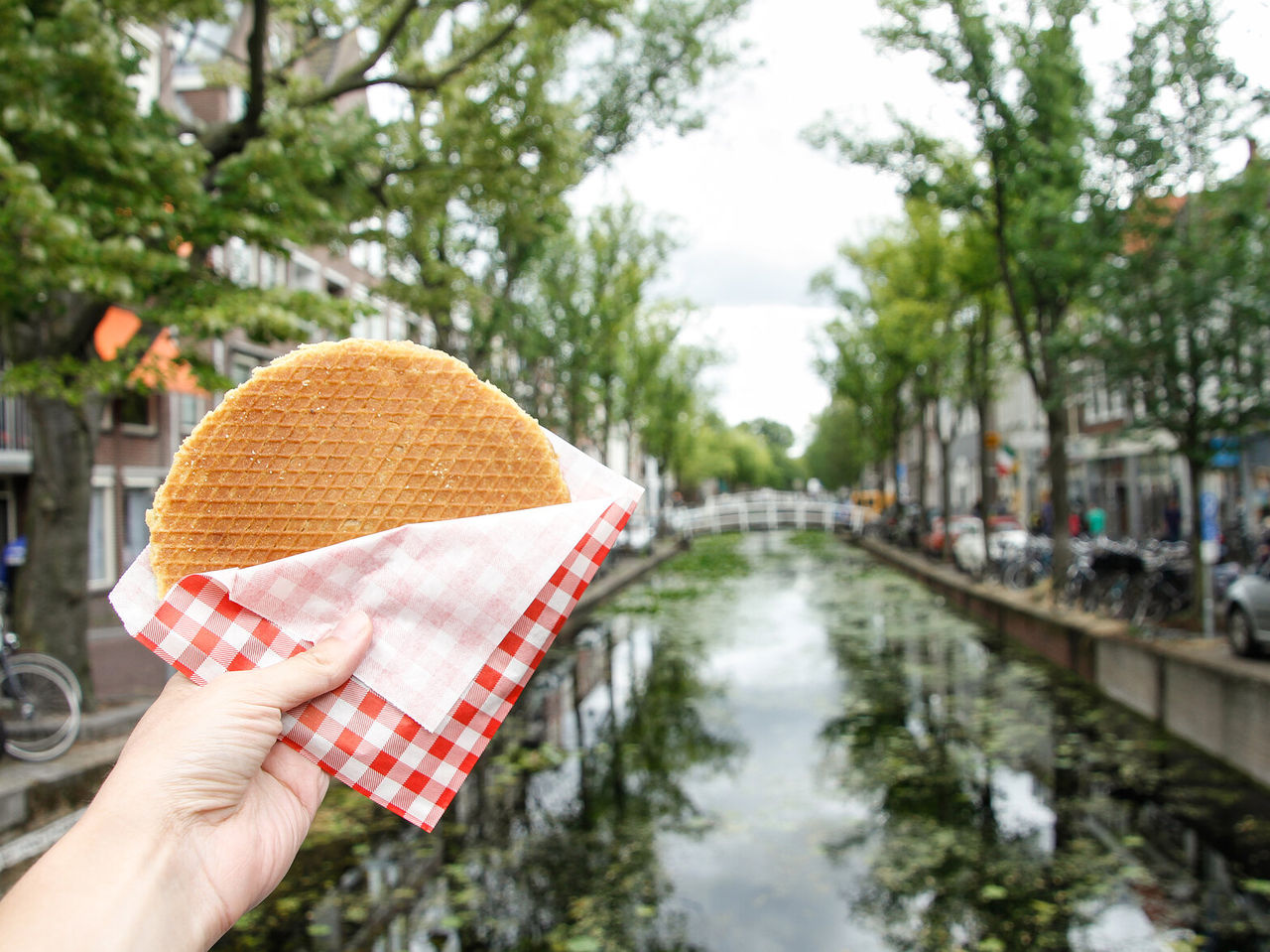 Mano sosteniendo una galleta holandesa, conocida como Stroopwafel, rellena de caramelo, con un canal de fondo