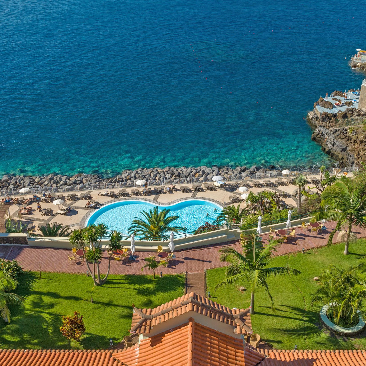 Vista aérea de Pestana Vila Lido Madeira, con vista al mar, palmeras alrededor y una piscina