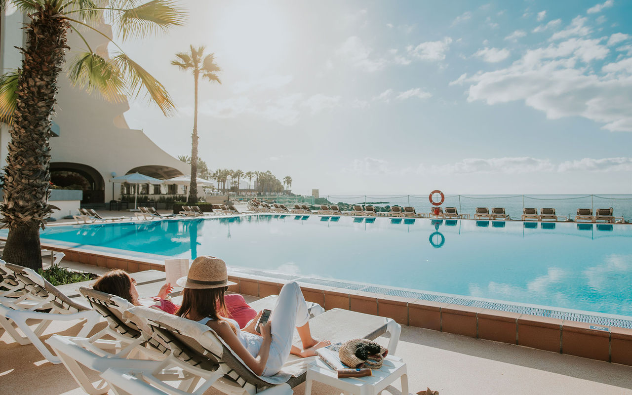 Personas disfrutando de la piscina exterior con vista al mar, en un hotel perteneciente a Pestana Hotels & Resorts