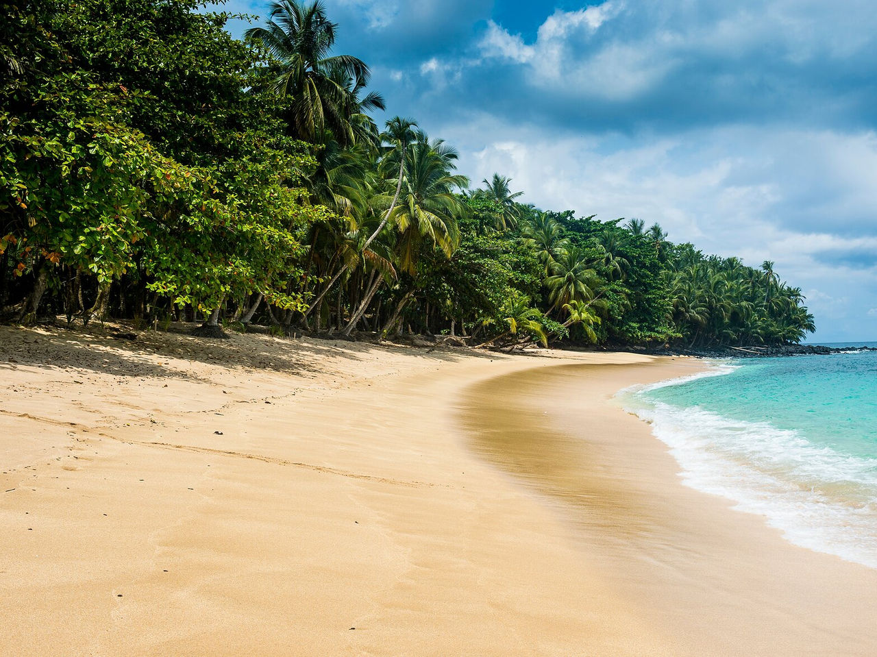 Plage déserte à São Tomé, avec une mer très bleue et calme, et une végétation dense entourant la plage