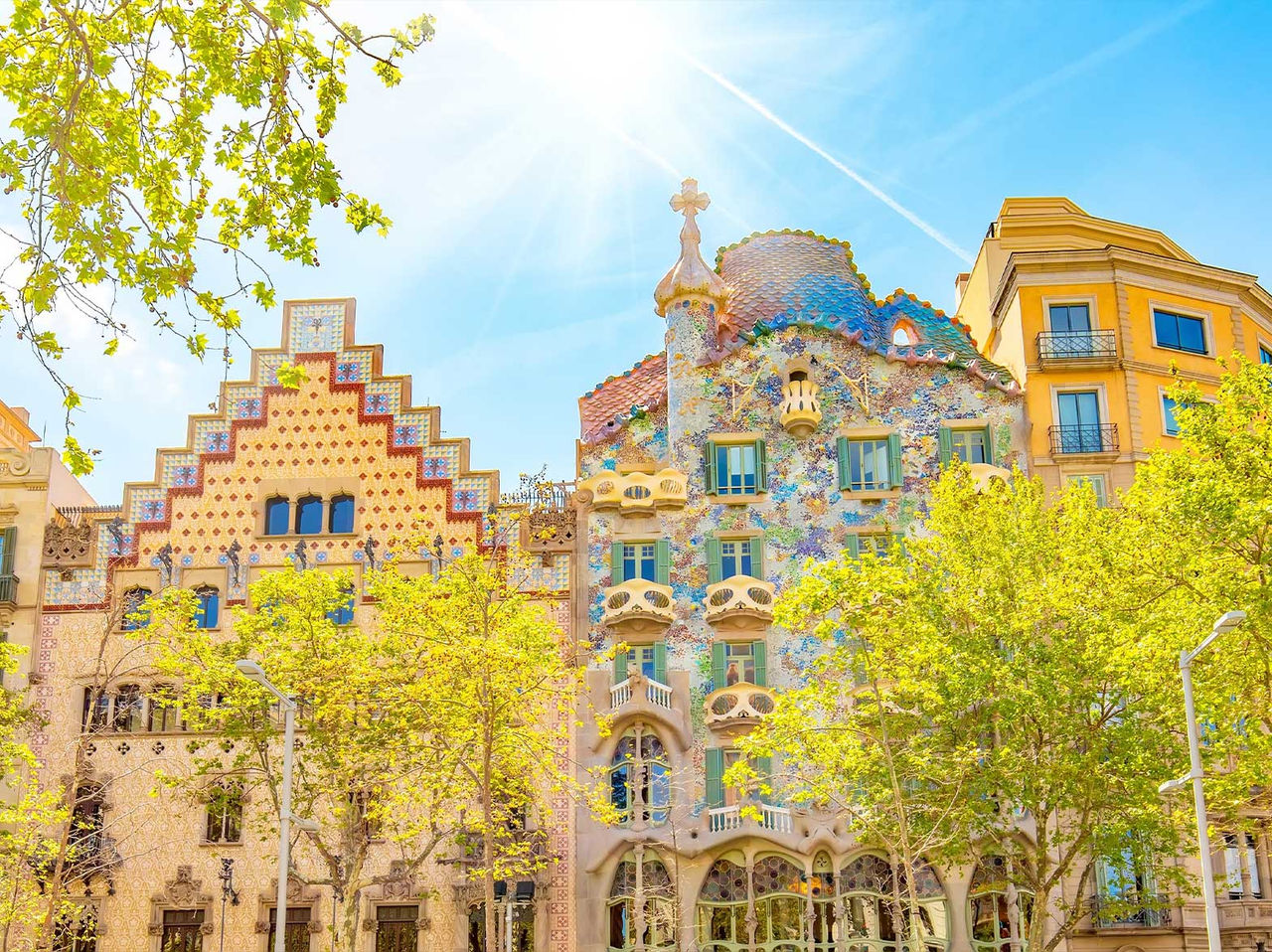 Édifice emblématique de la Casa Batlló de Gaudí à Barcelone, avec sa façade colorée, entouré d'arbres en fleurs