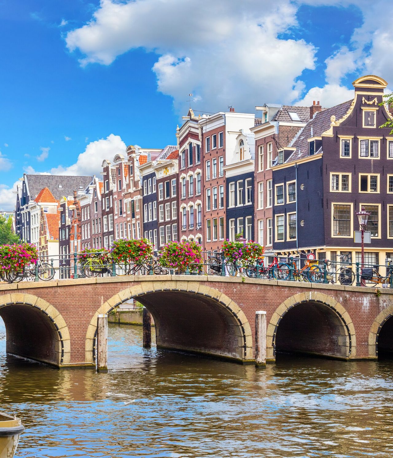 Pont piétonnier sur un canal à Amsterdam, avec des vélos garés, des fleurs colorées et des bâtiments en arrière-plan