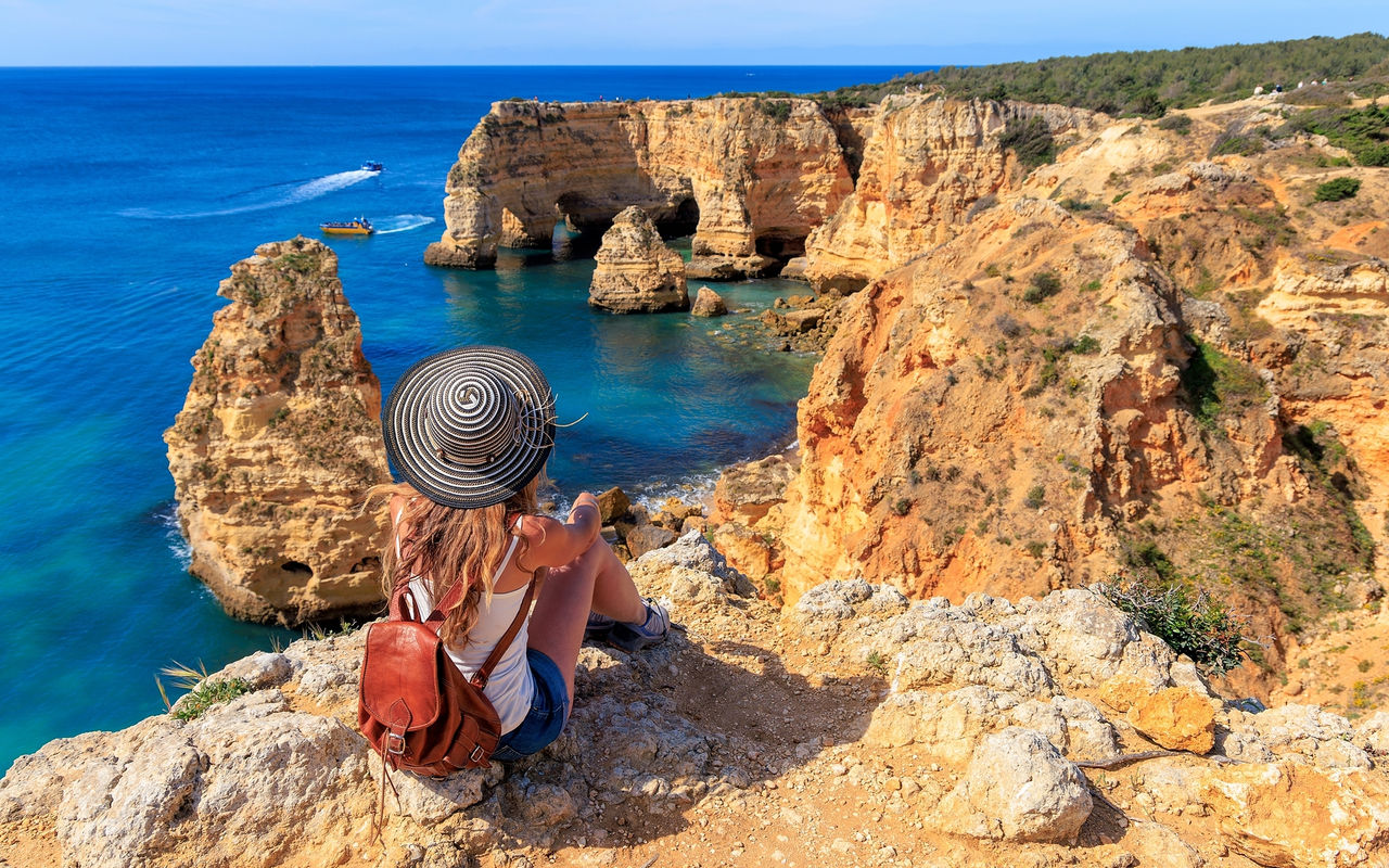 Femme admirant la vue panoramique de la côte de l'Algarve, avec des eaux cristallines et une falaise entourée de végétation
