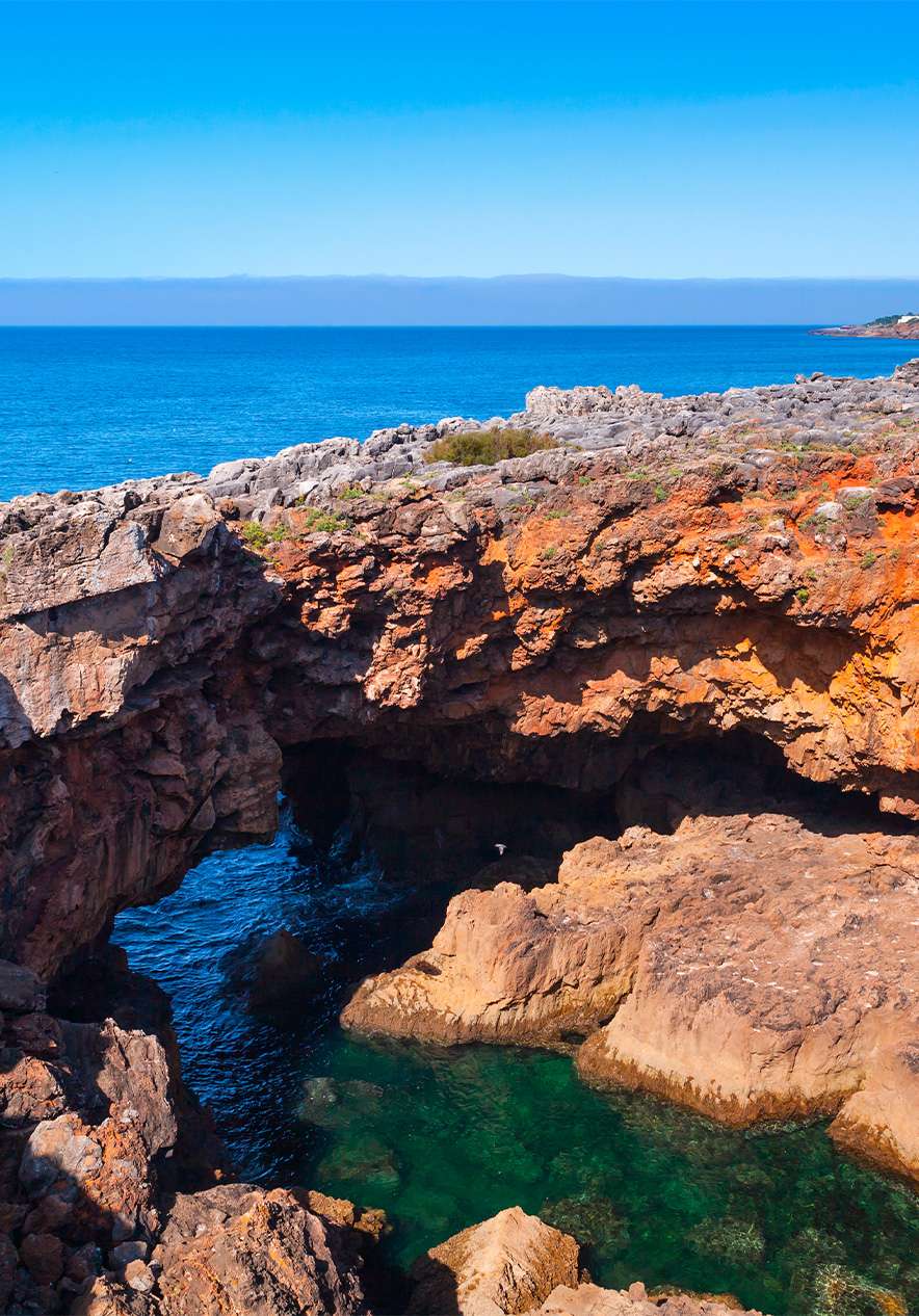 La mer bleue rencontre des roches imposantes, créant un contraste entre l'eau calme et la robustesse des roches