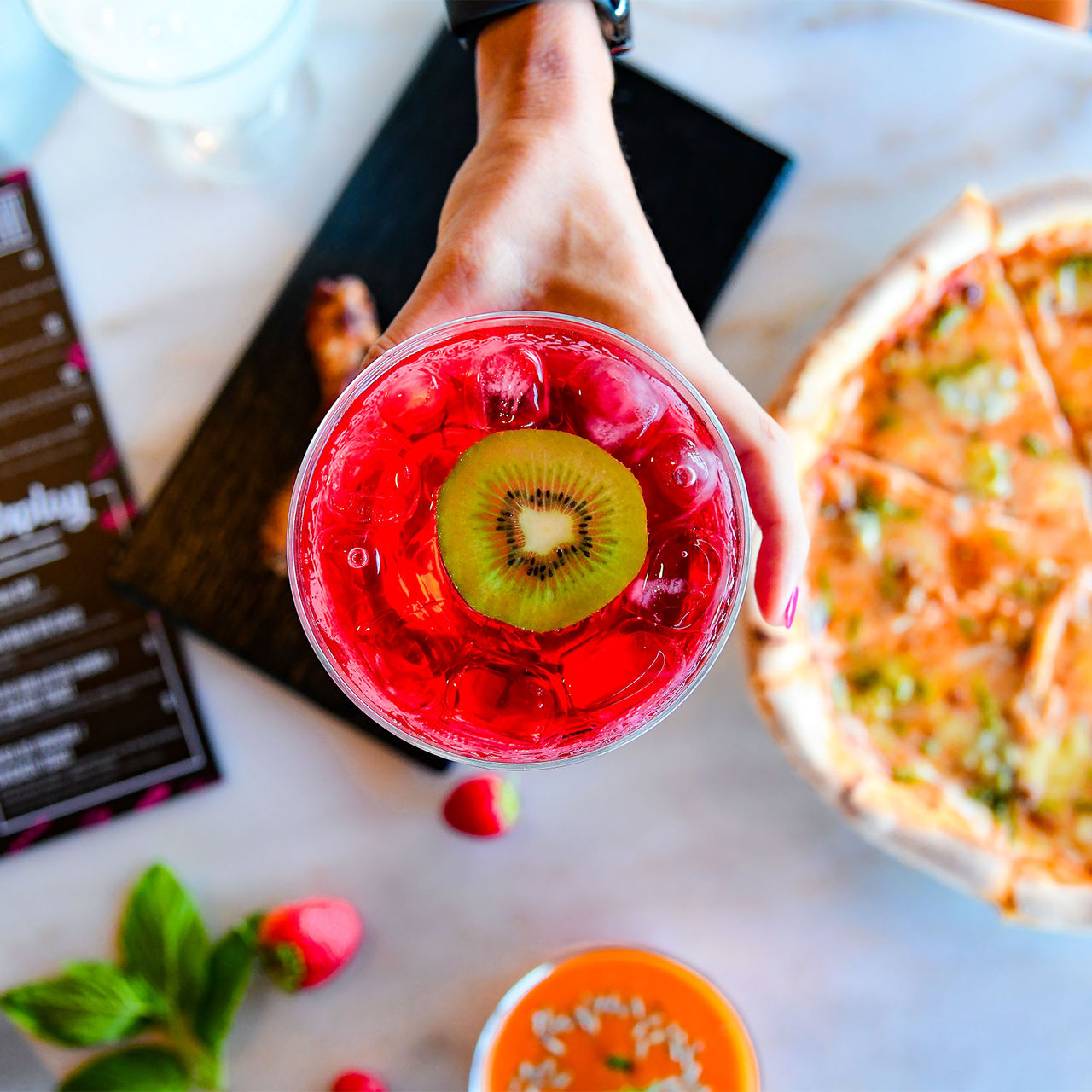 Vue du haut d'un cocktail rose avec une rondelle de kiwi accompagnant une pizza au Pestana CR7 Funchal