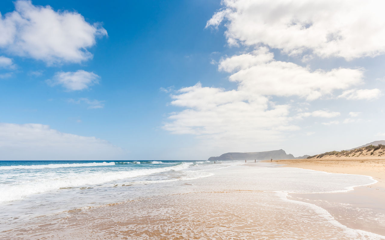 Plage étendue à Porto Santo avec du sable clair, des vagues calmes et un ciel bleu avec quelques nuages