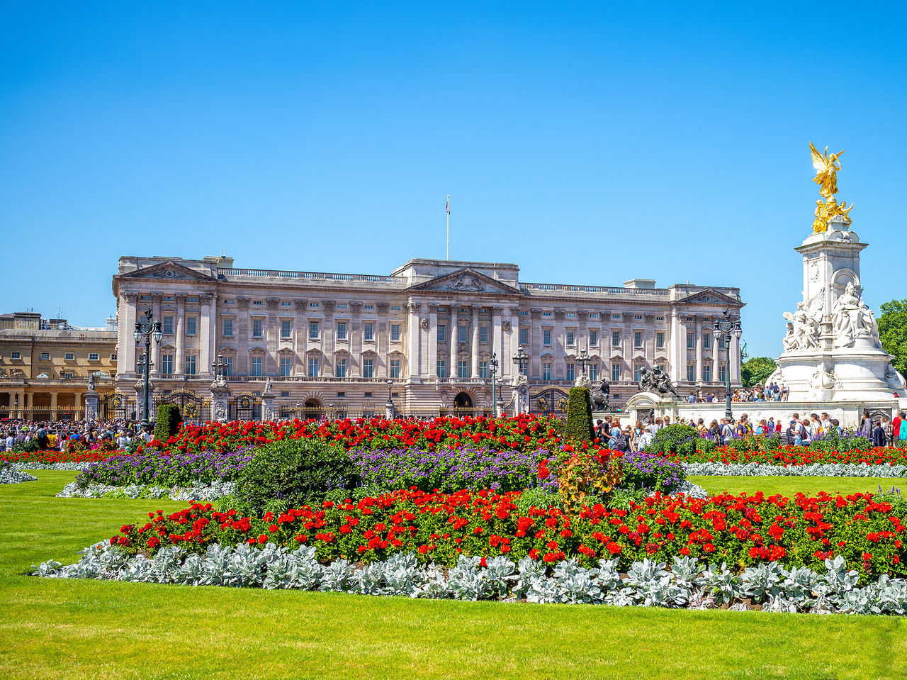 L'imposante façade du palais de Buckingham à Londres, avec une statue dorée et un jardin fleuri devant