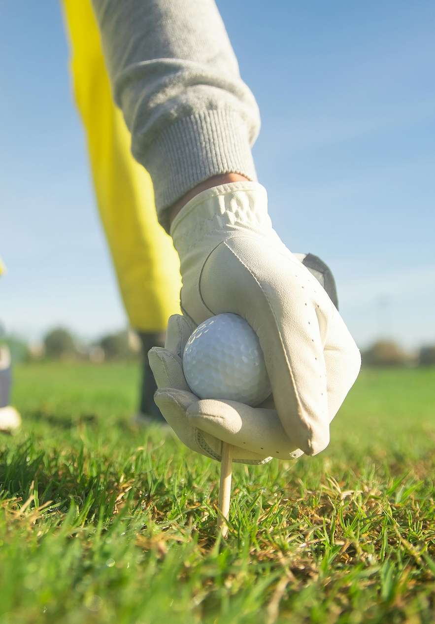 Personne sur un terrain de golf plaçant la balle sur un tee, vêtu de gants blancs, de pantalons jaunes