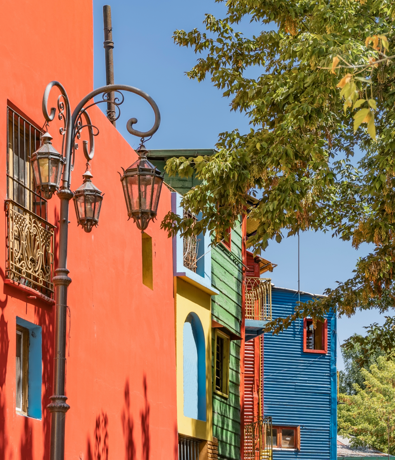 Bâtiments colorés dans le quartier typique de Caminito à Buenos Aires, avec des arbres devant et un ciel bleu derrière