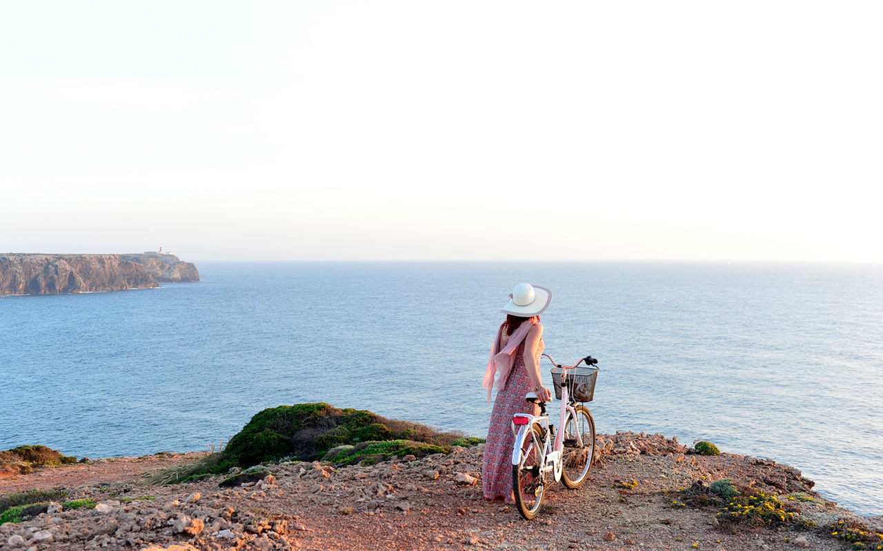 Femme se promenant avec un vélo à la main, le long des falaises de la côte portugaise, fourni par Pousadas de Portugal