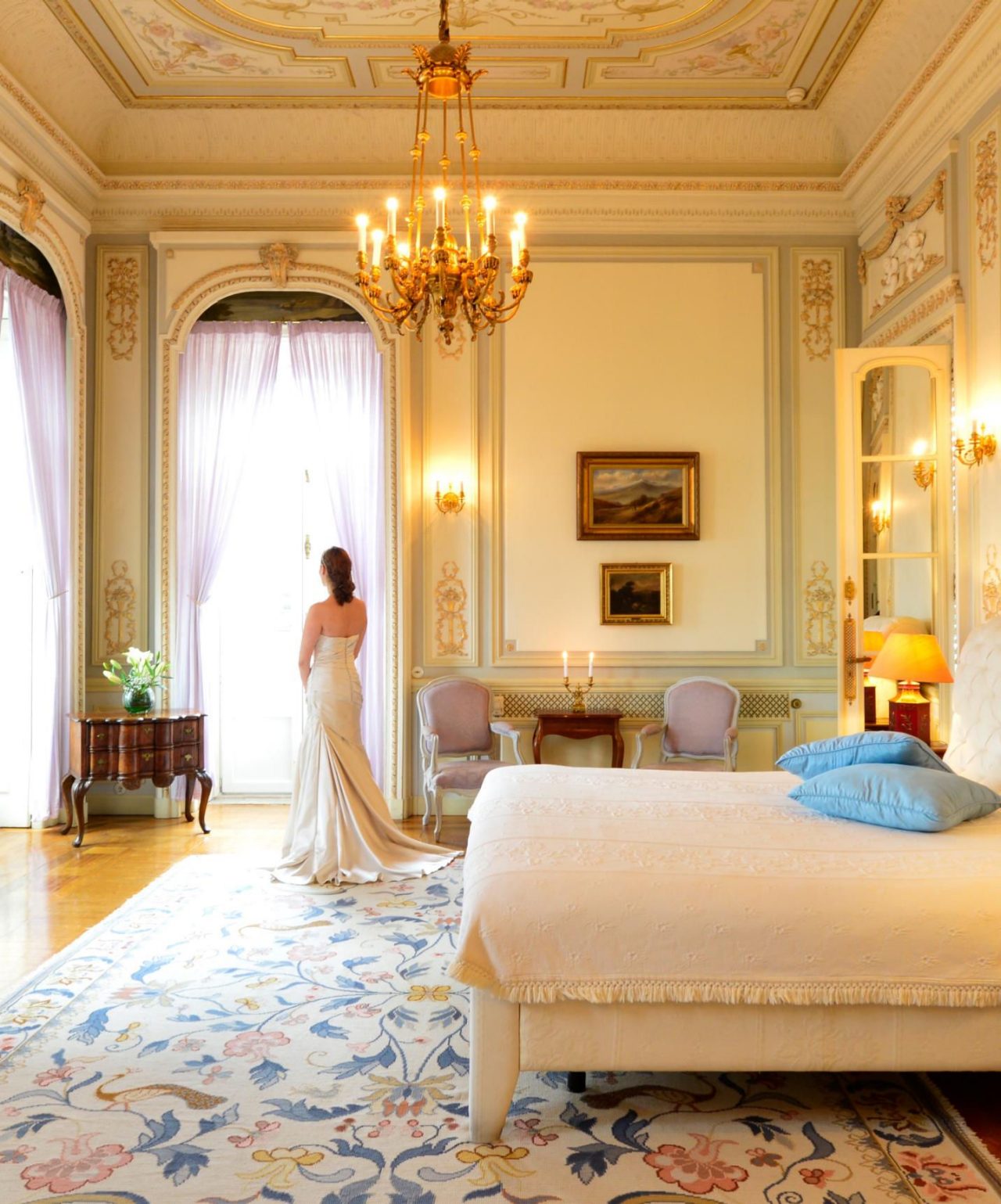 La mariée se prépare pour son mariage dans une chambre d'hôtel élégante, avec des murs ornés de détails dorés et un lustre en cristal