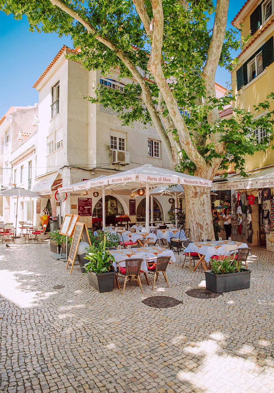 Een restaurant op het Largo do Camões in Cascais, met tafels onder een grote boom op een zonnige dag