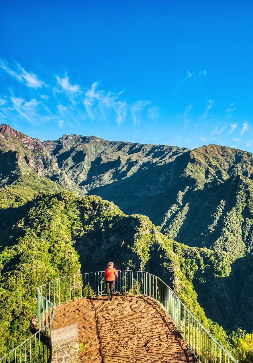 Een persoon wandelt en stopt om van het groene berglandschap te genieten vanaf een uitkijkpunt op Madeira