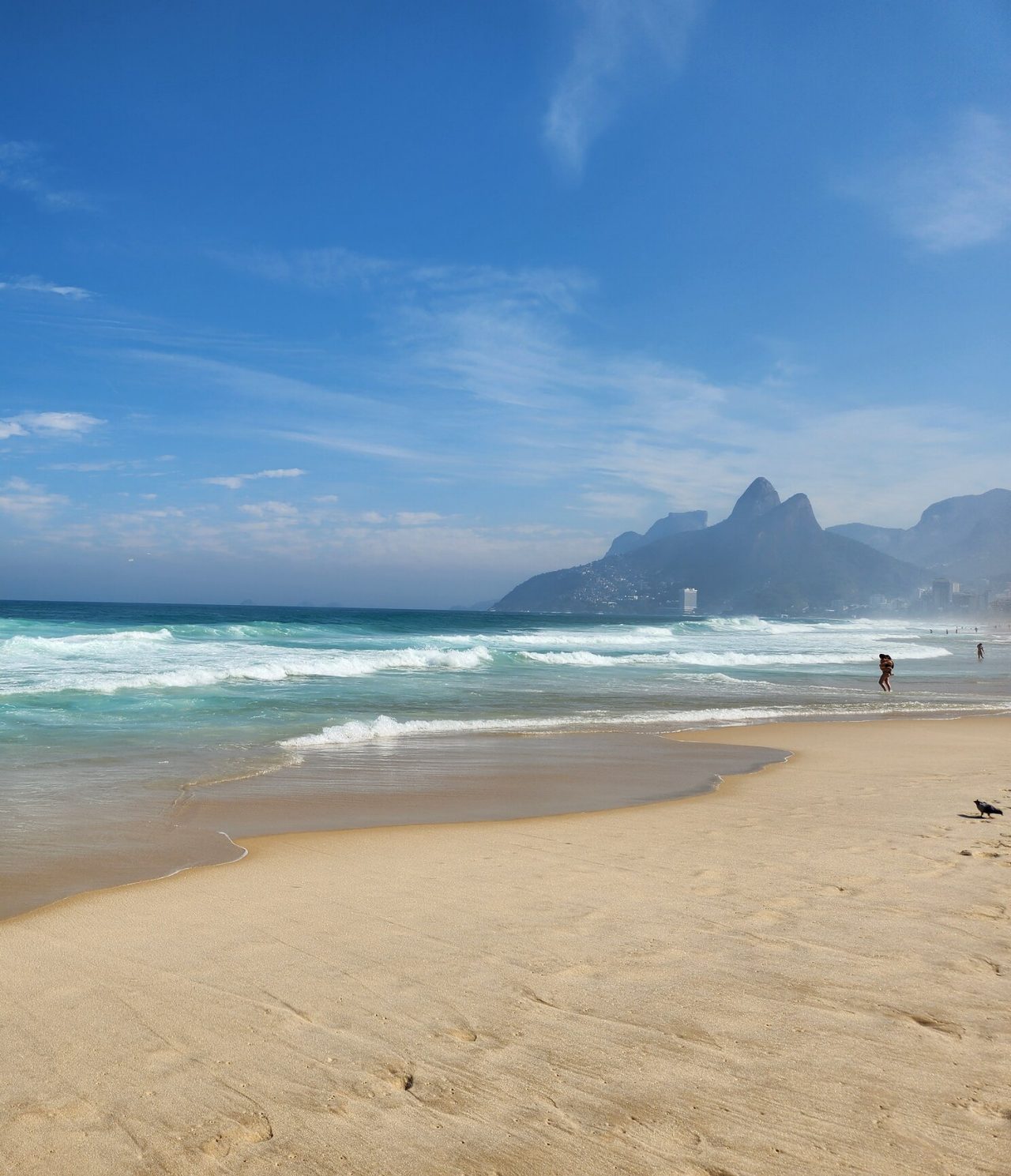 Uitzicht op een strand in Rio de Janeiro, met wit zand, turkoois water, bergen en mensen aan de waterkant