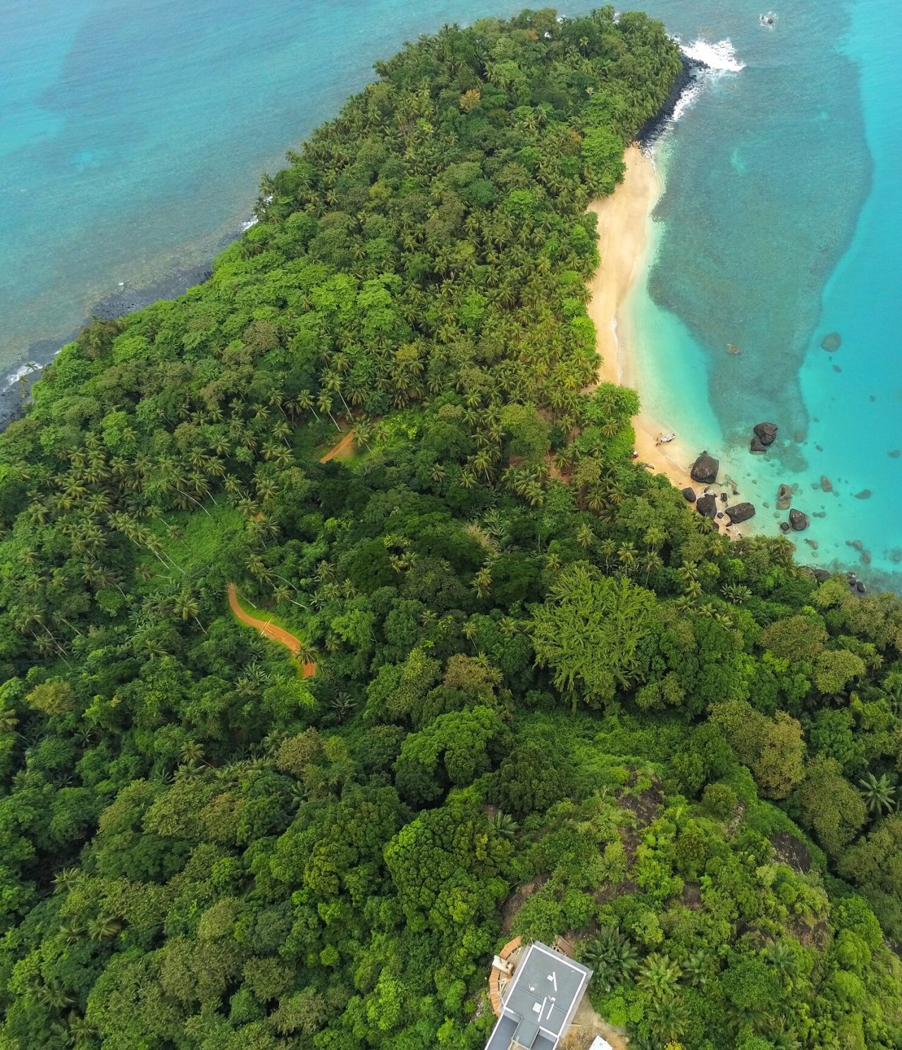 Vista aérea da ilha de São Tomé e Príncipe, com muita vegetação, uma praia de areia branca deserta e águas cristalinas